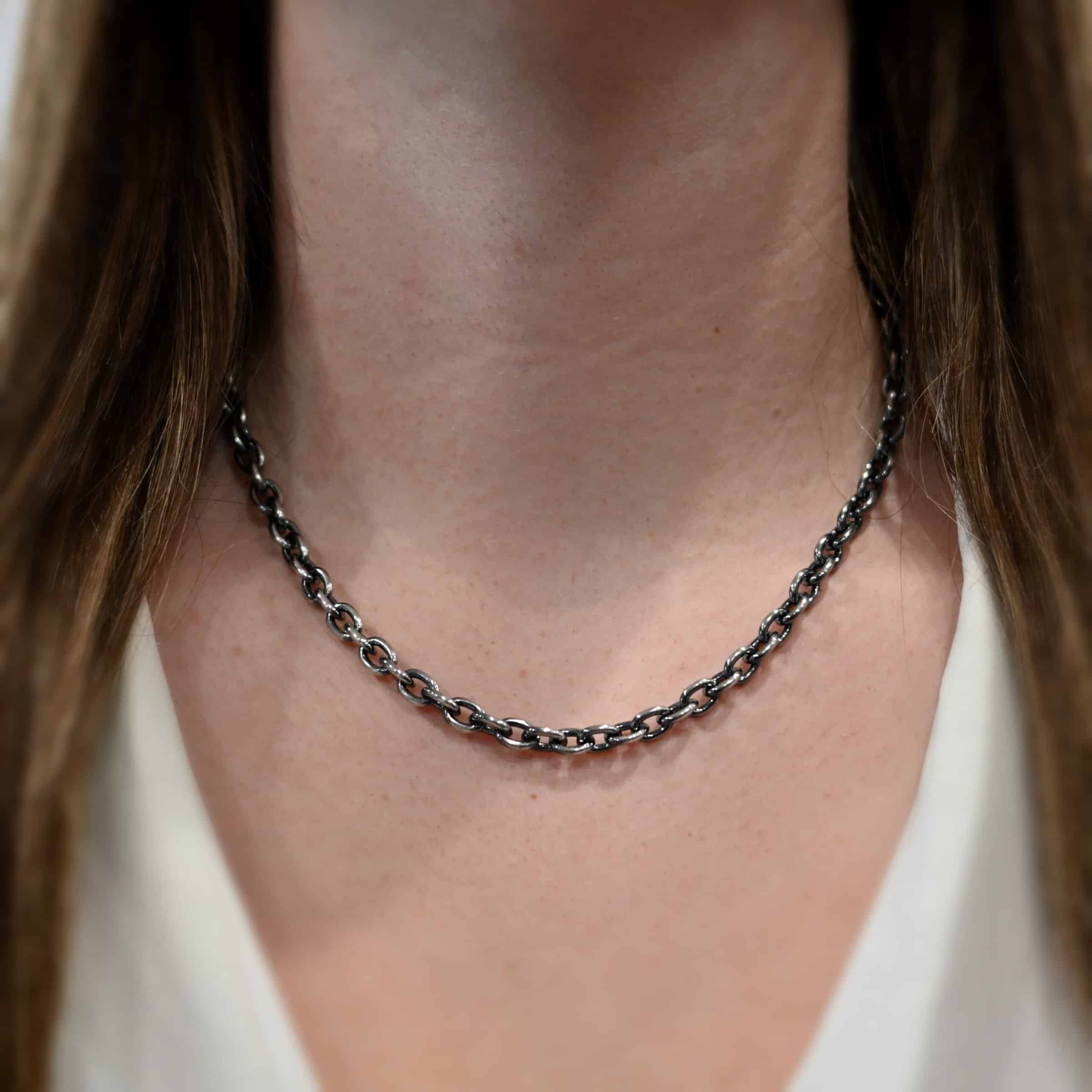 Close up of the "Georgia" Chain worn on a model. Heavy links measure 8x6mmx1.7mm thick. Chain is shown at 18" long and oxidized on a model. Model is wearing a white v-neck shirt.