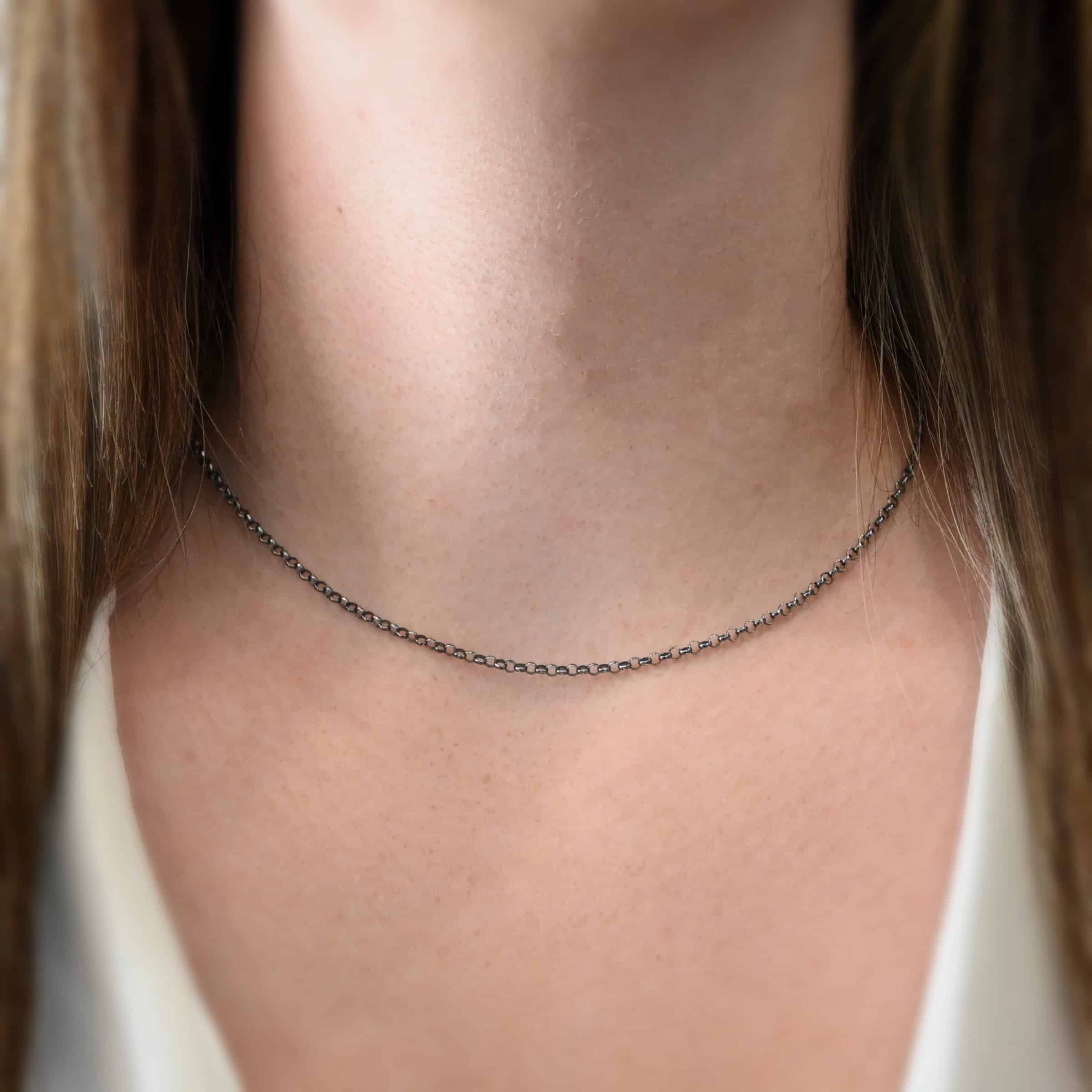 Close up of the "Rachel Rolo" Chain. Chain is shown at 16" long and oxidized. Chain is made out of sterling silver. Chain is small but thick circle links connected together. Model is wearing a white v-neck shirt.