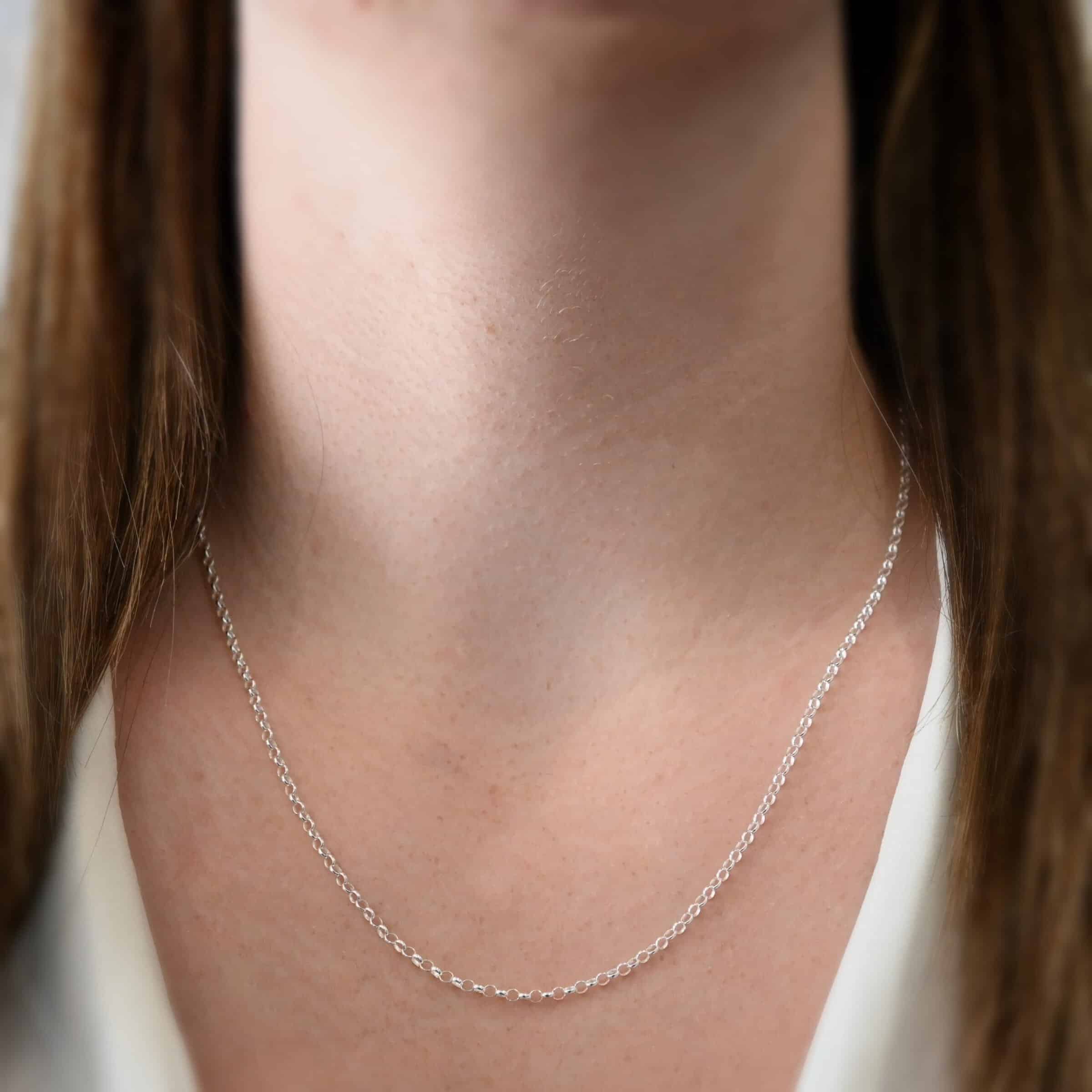Close up of the "Rachel Rolo" Chain. Chain is shown at 20" long and shiny. Chain is made out of sterling silver. Chain is small but thick circle links connected together. Model is wearing a white v-neck shirt.