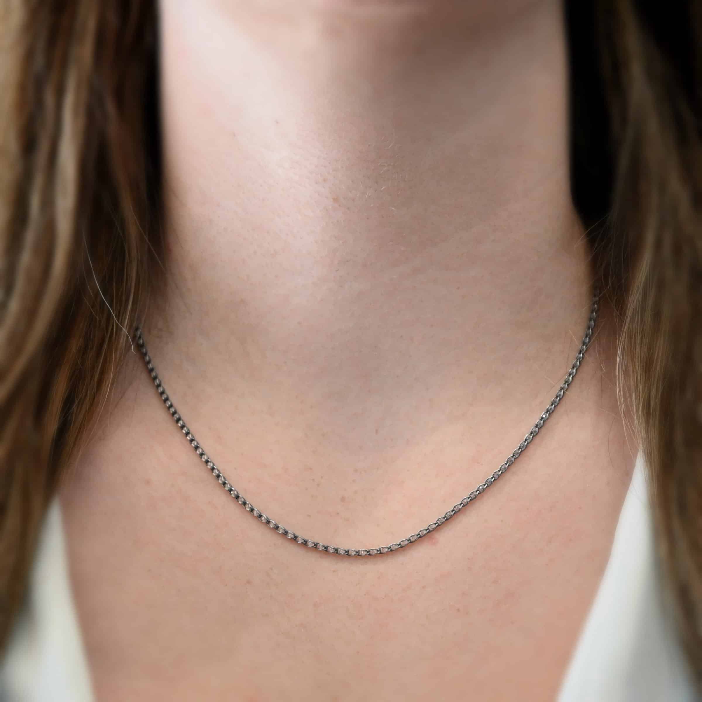 Scarlett 18-20" Oxidized Close up of the "Scarlett" Chain. Chain is shown at 18" long and oxidized. Chain is made out of sterling silver and has many cubic zirconia stones that are inside of the chain. The cz's have no space between them, and they go all the way around the chain. Model is wearing a white v-neck shirt.