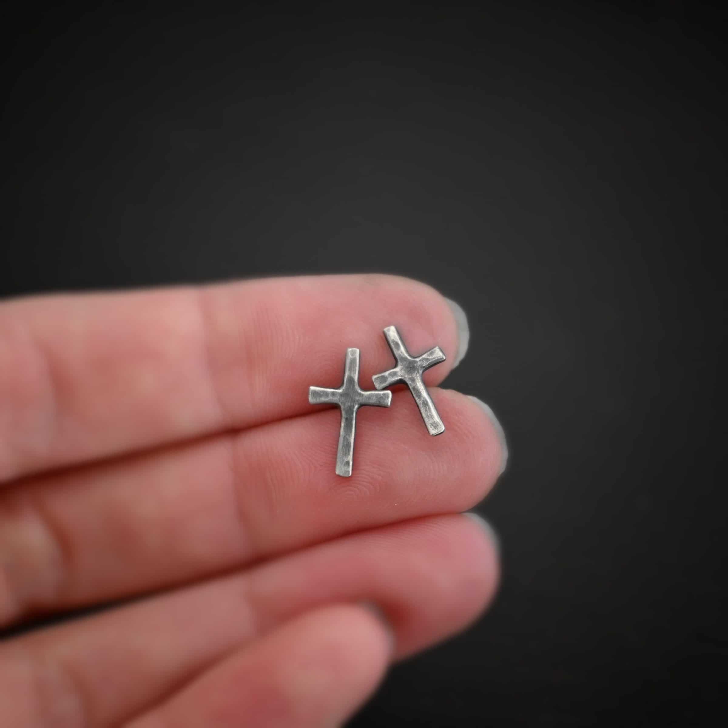 Healer Earrings Photo of the "Healer" earrings. The small crosses are hammered and oxidized, with posts on the back of them. Earrings are held in between the fingertips of a hand.