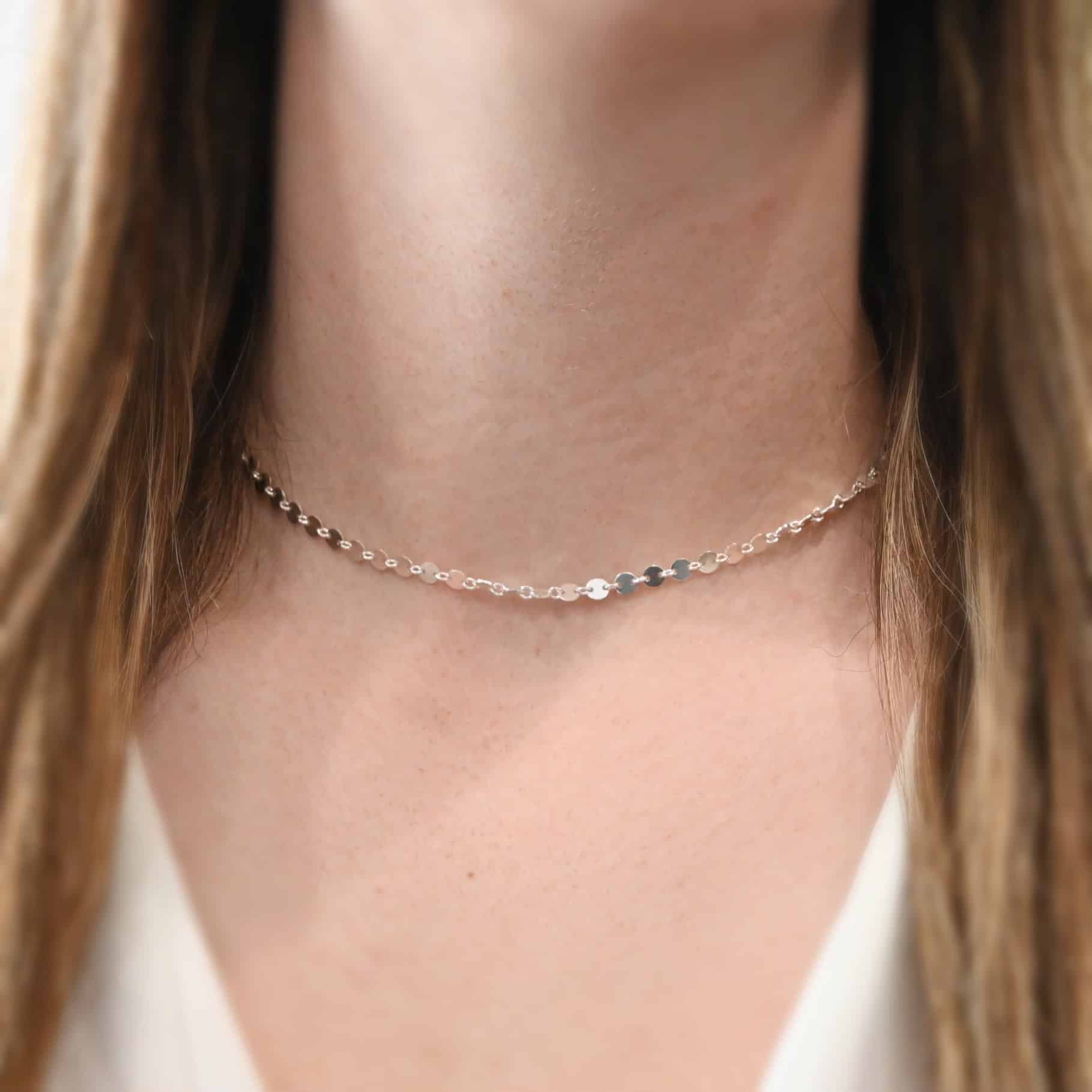"Gypsy Coin" Chain as shown on a model. Chain is shown at 15" long and as shiny sterling silver. 4mm disks connected with jump rings. Model is wearing a white v-neck shirt.