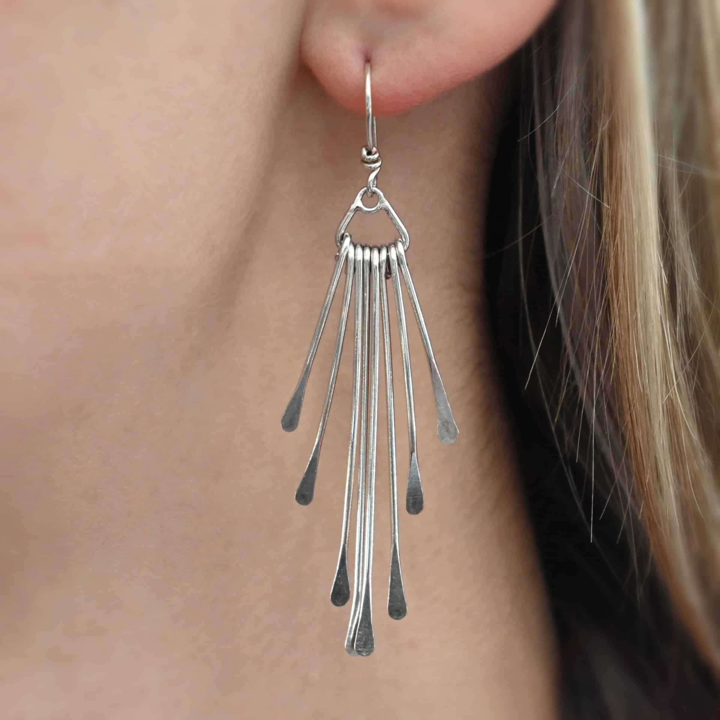 Photo of the "Marilyn Monroe" Earring as shown up close by a model. Made out of sterling silver. Earrings have french hook ear wires. Attached to the bottom loop of the ear wires is a teardrop shaped piece of silver. Hanging from this piece are eight separate pieces of silver, all with hammered paddle ends. They all hang straight down. The shortest ones are on the outside, and they get progressively longer until the middle. So they go from short, to long, and back to short.
