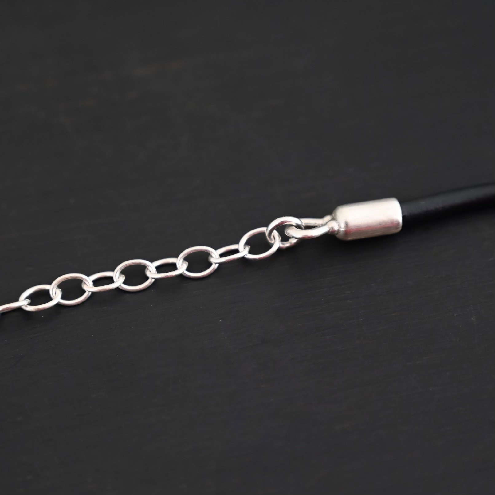 Close up of the end cap for the "Wren Wire" Chain. This chain is made out of leather, and has a shiny sterling silver end cap with a sterling silver extension on it.
