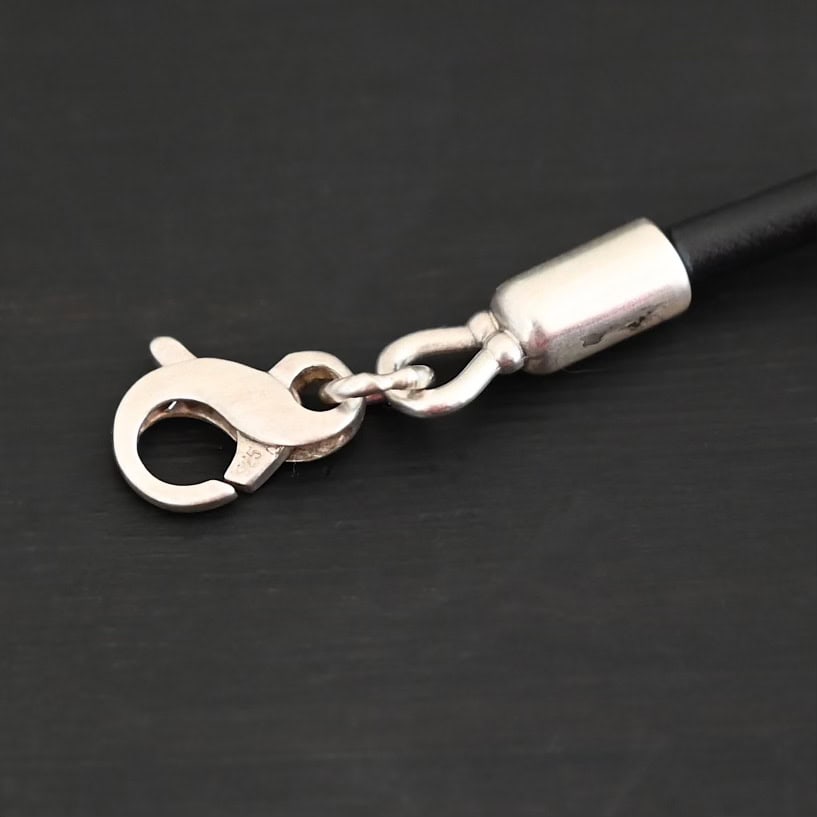Close up of the "Wren Wire" Clasp. This is the clasp for the "Wren Wire" Chain, which is made out of leather. It has an infinity clasp on it that is sterling silver and shiny.