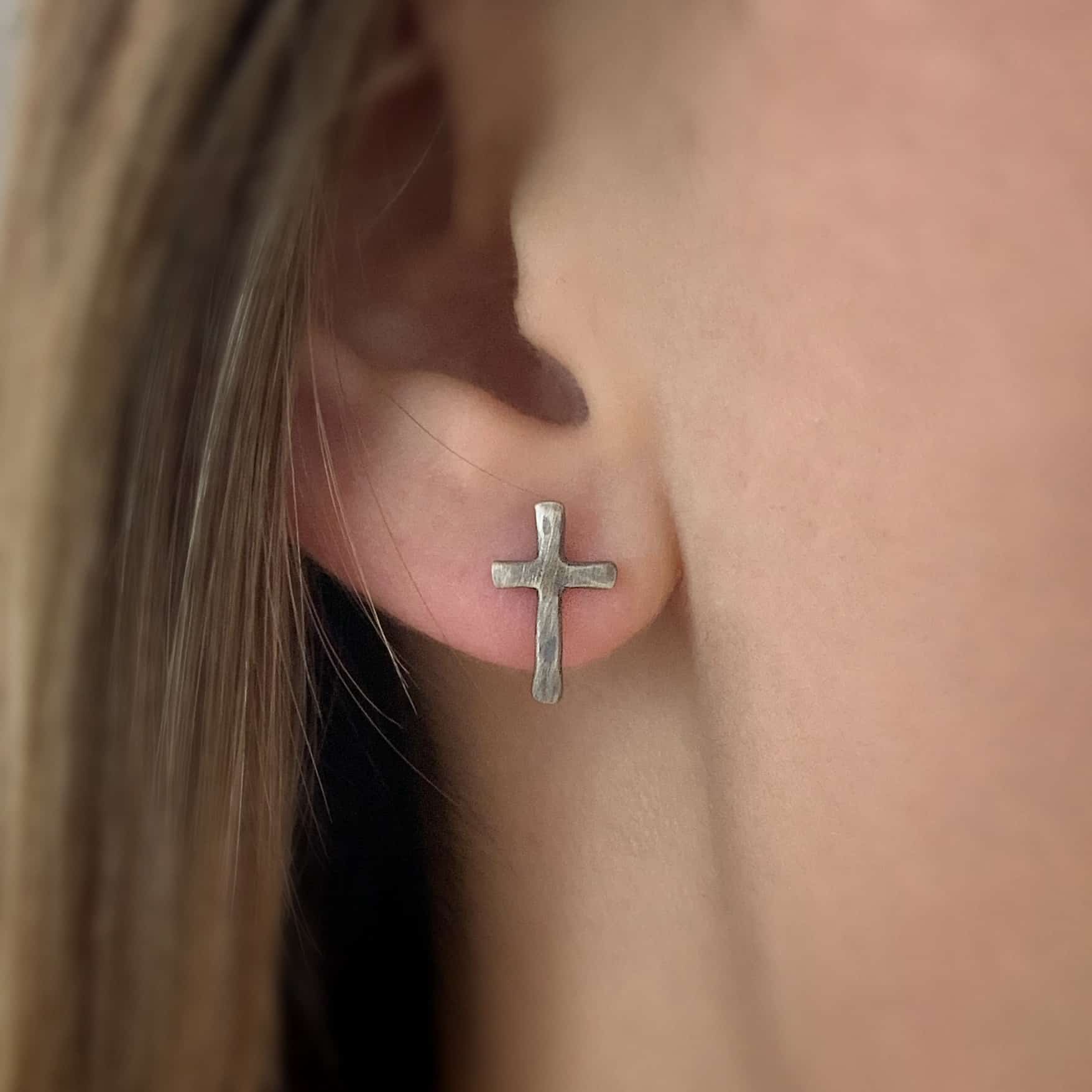 Healer Earrings 3 Photo of the "Healer" Earring as shown on a model. Earring is oxidized and made out of sterling silver. The earrings are cross earrings with posts on the back center of the cross. The crosses are hammered and oxidized.