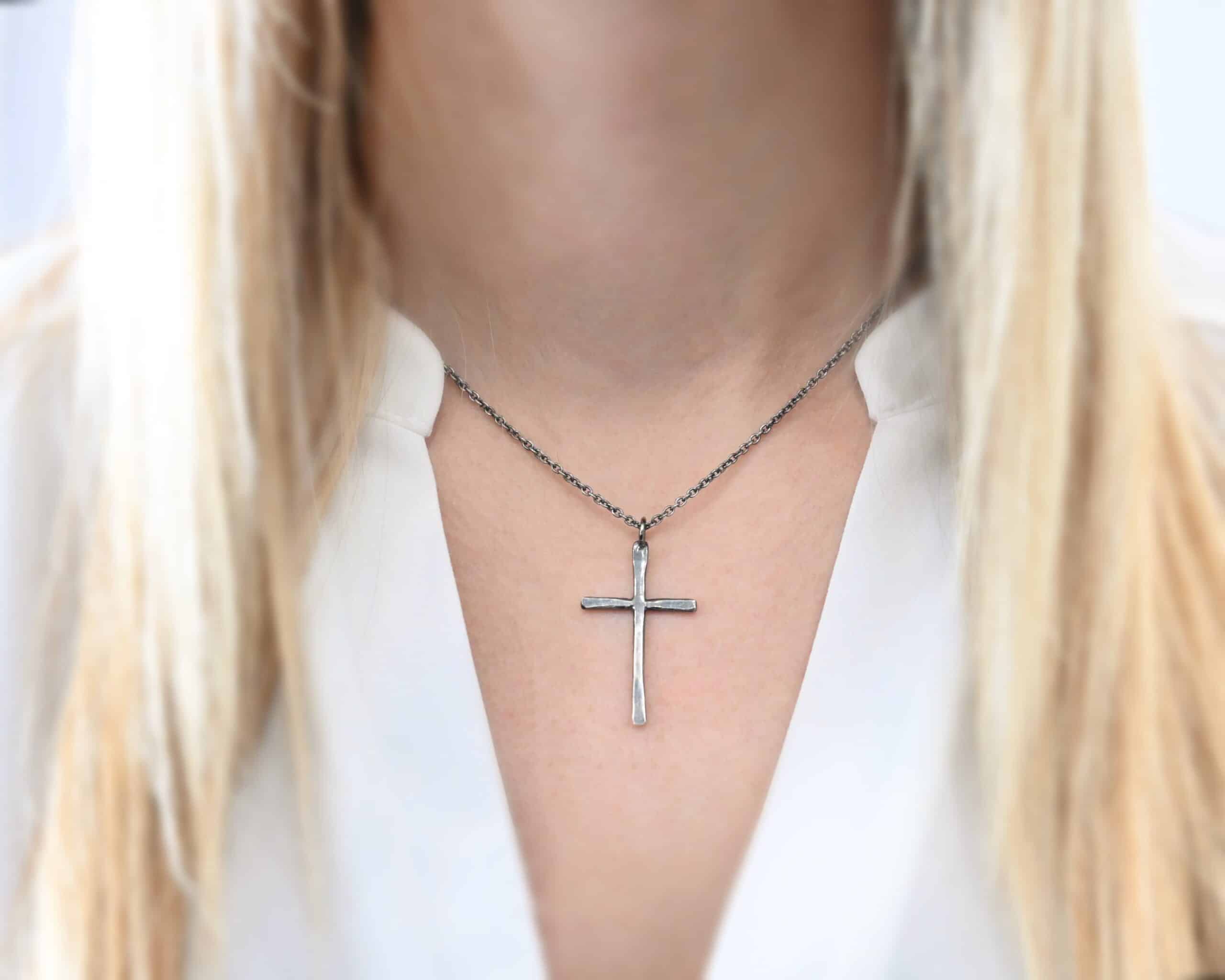 Photo of the "Healer" Necklace. Made out of sterling silver. There is a medium sized cross that is hammered flat, but smooth. It is oxidized and has a loop soldered to the top of it. There is a chain that goes through the top of the necklace. Necklace is worn by a model.
