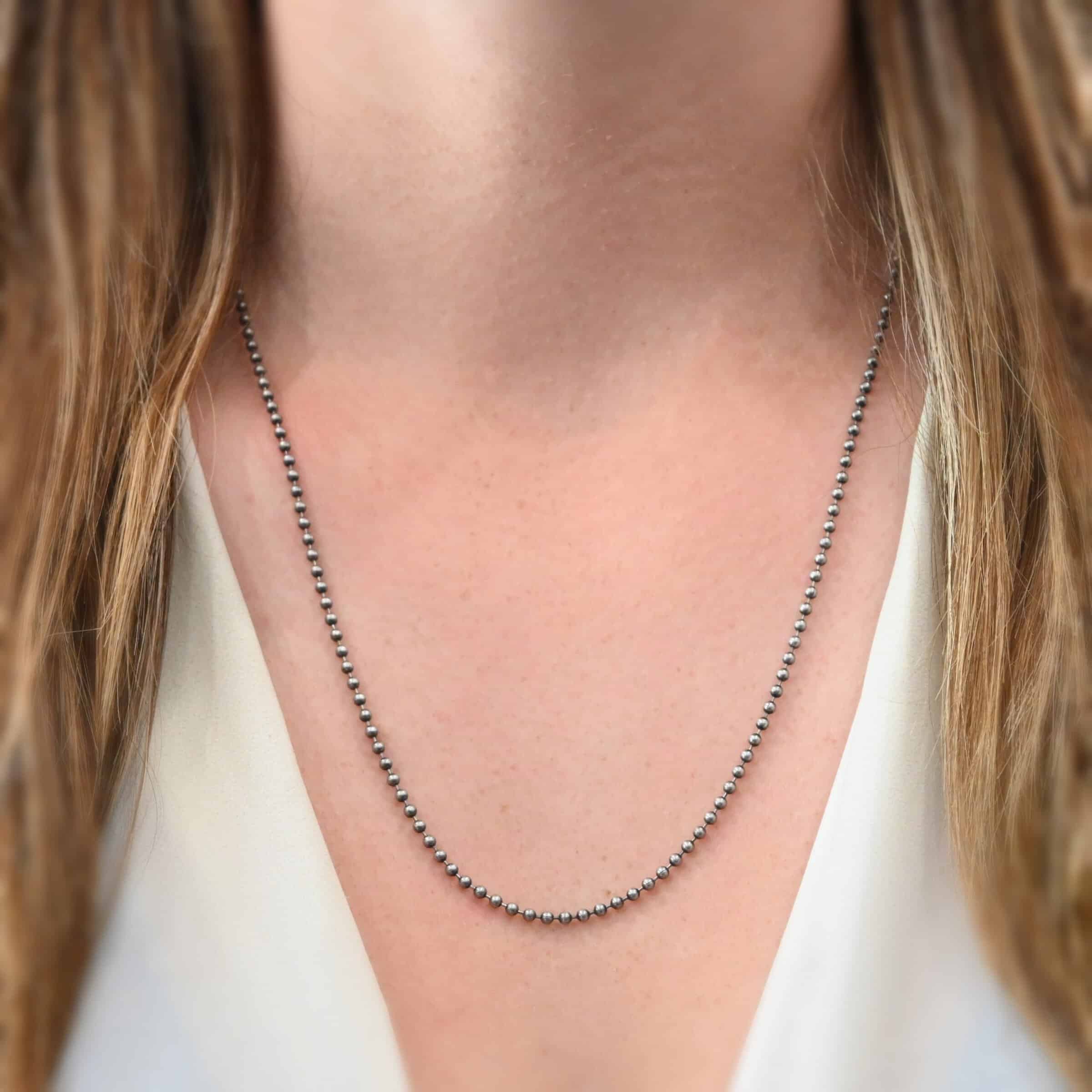 Beau Ball Chain, 22-24", 2.4mm Close up of the "Beau Ball" Chain as shown on a model. Made out of brushed stainless steel with 2.4 mm balls that are spaced apart evenly on the chain. Chain is shown worn on a model at 22 inches long. Model is wearing a white v-neck shirt.