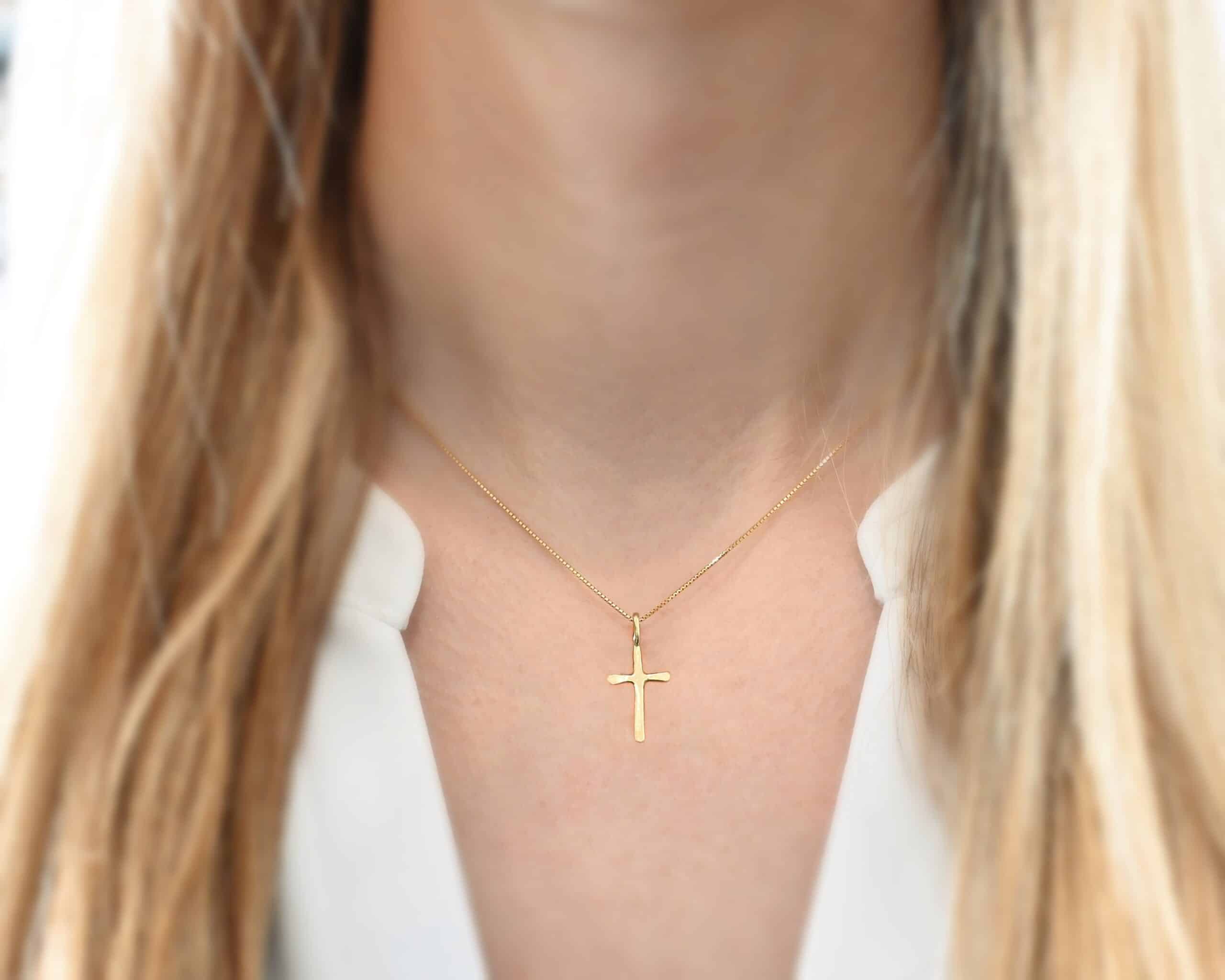 Divine Necklace Photo of the "Divine" Necklace. Made out of 18k gold. There is a small sized cross that is flat and smooth. It has a loop soldered to the top of it. There is a chain that goes through the loop of the cross that is also gold. Necklace is worn by a model to demonstrate size.