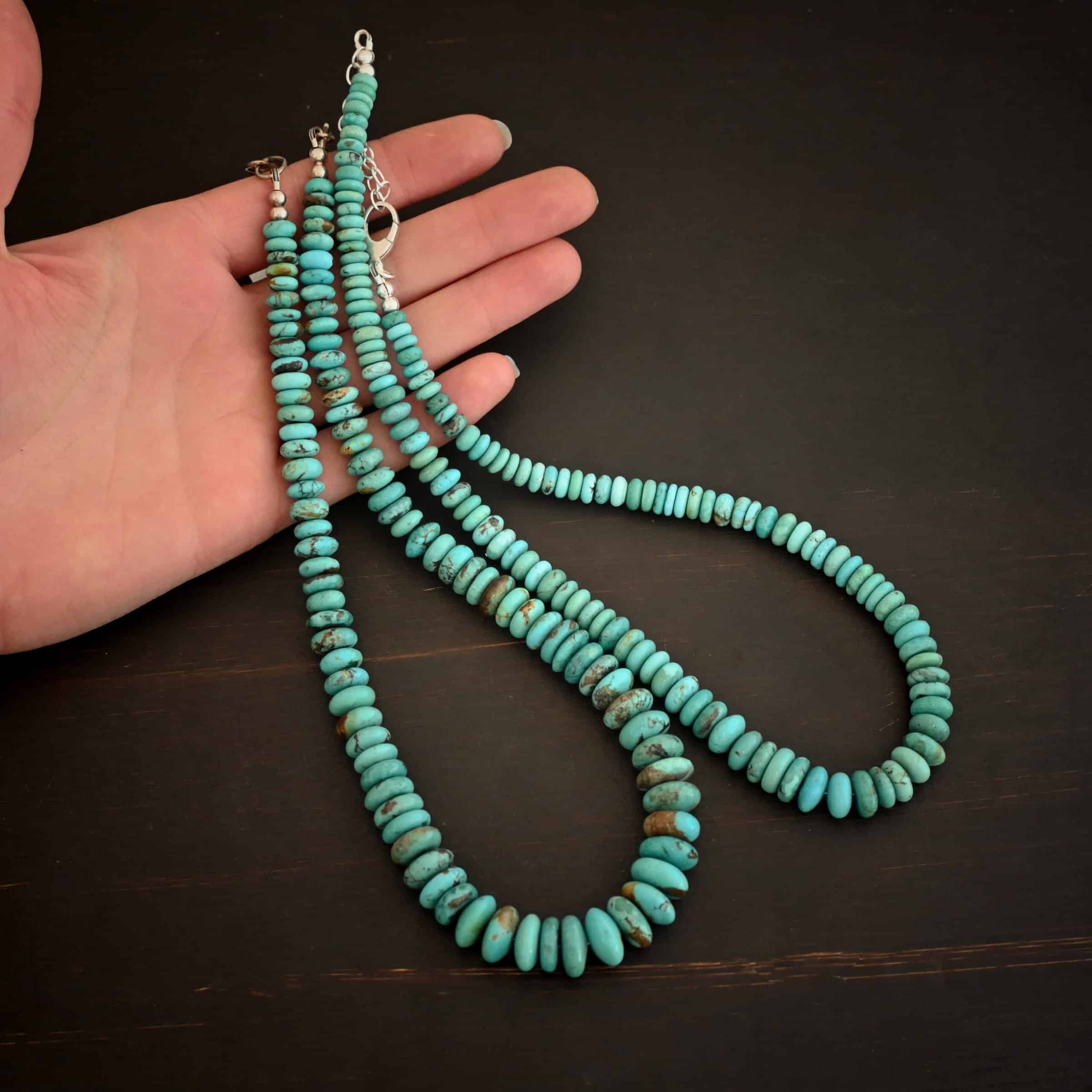 Bonnie Necklace Photo of the "Bonnie" Necklace shown in different sized beads. Made out of sterling silver and turquoise. Beads are varying shades of blueish green colors. The beads graduate in size as they get towards the center. Beads are strung tightly together. The left necklace is larger than the right. Necklaces are lying against the fingertips of a hand to demonstrate size.