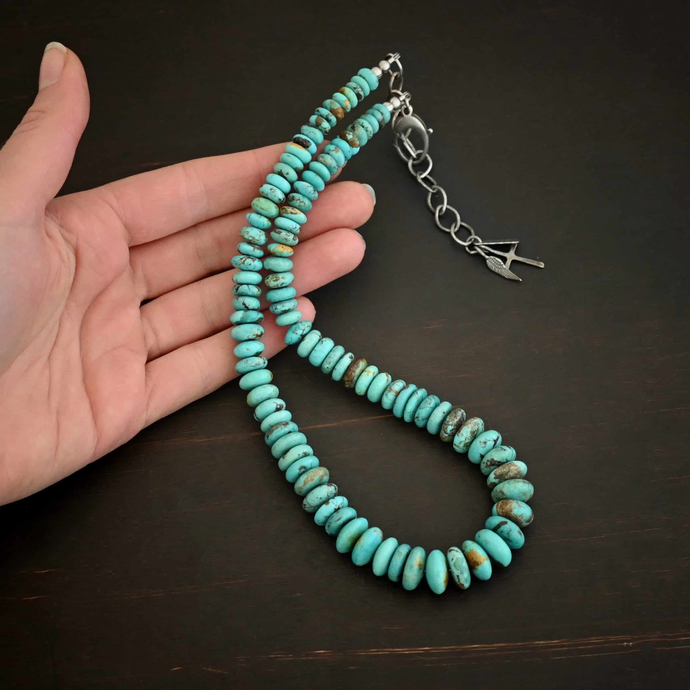 Bonnie Large Photo of the "Bonnie" Necklace. Made out of sterling silver and turquoise. Beads are varying shades of blueish green colors. The beads graduate in size as they get towards the center. Beads are strung tightly together. Necklace is lying against the fingertips of a hand.