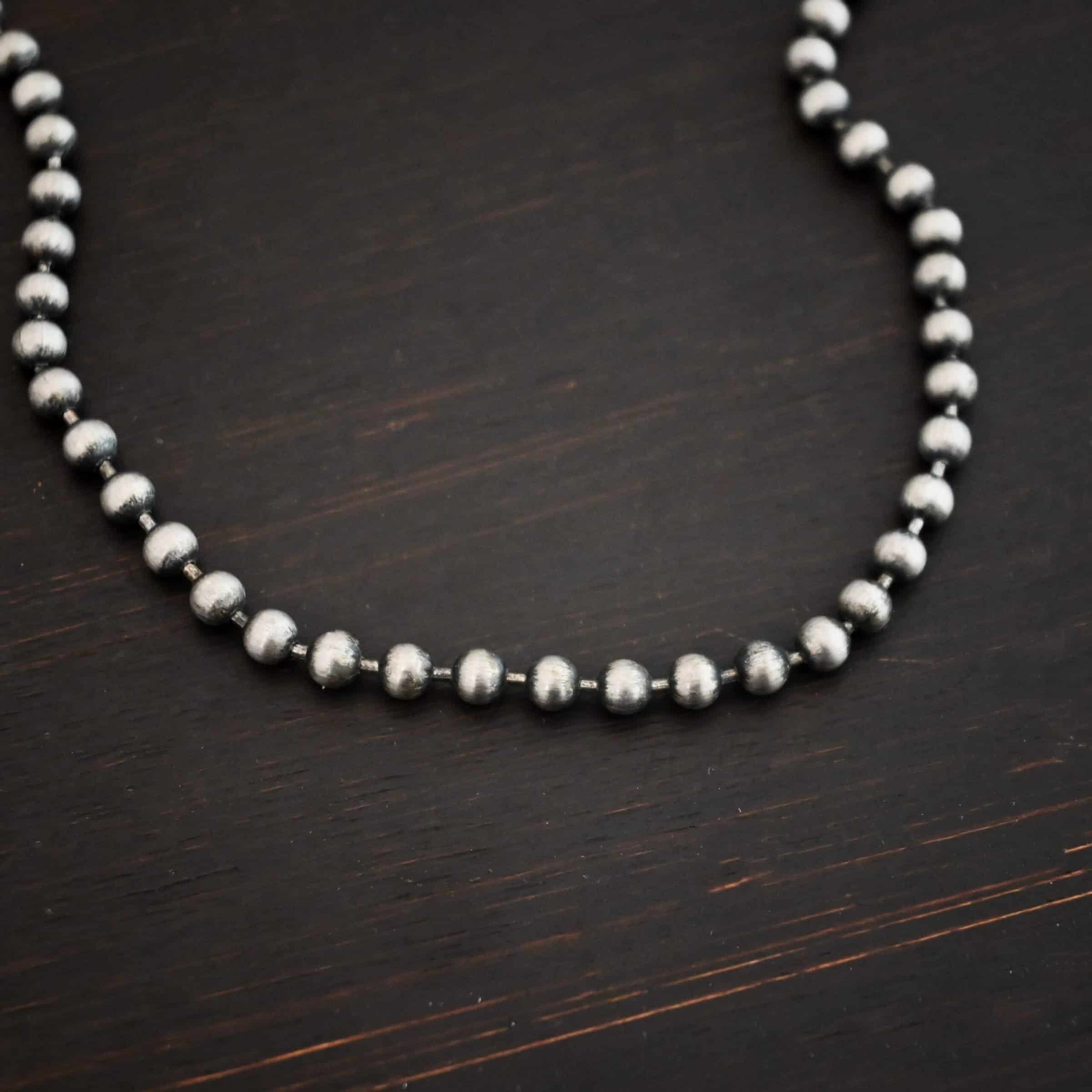 Beau Ball Chain Close up of the "Beau Ball" Chain. Made out of brushed stainless steel with 4mm balls that are spaced apart evenly on the chain. Chain is set against a dark background.