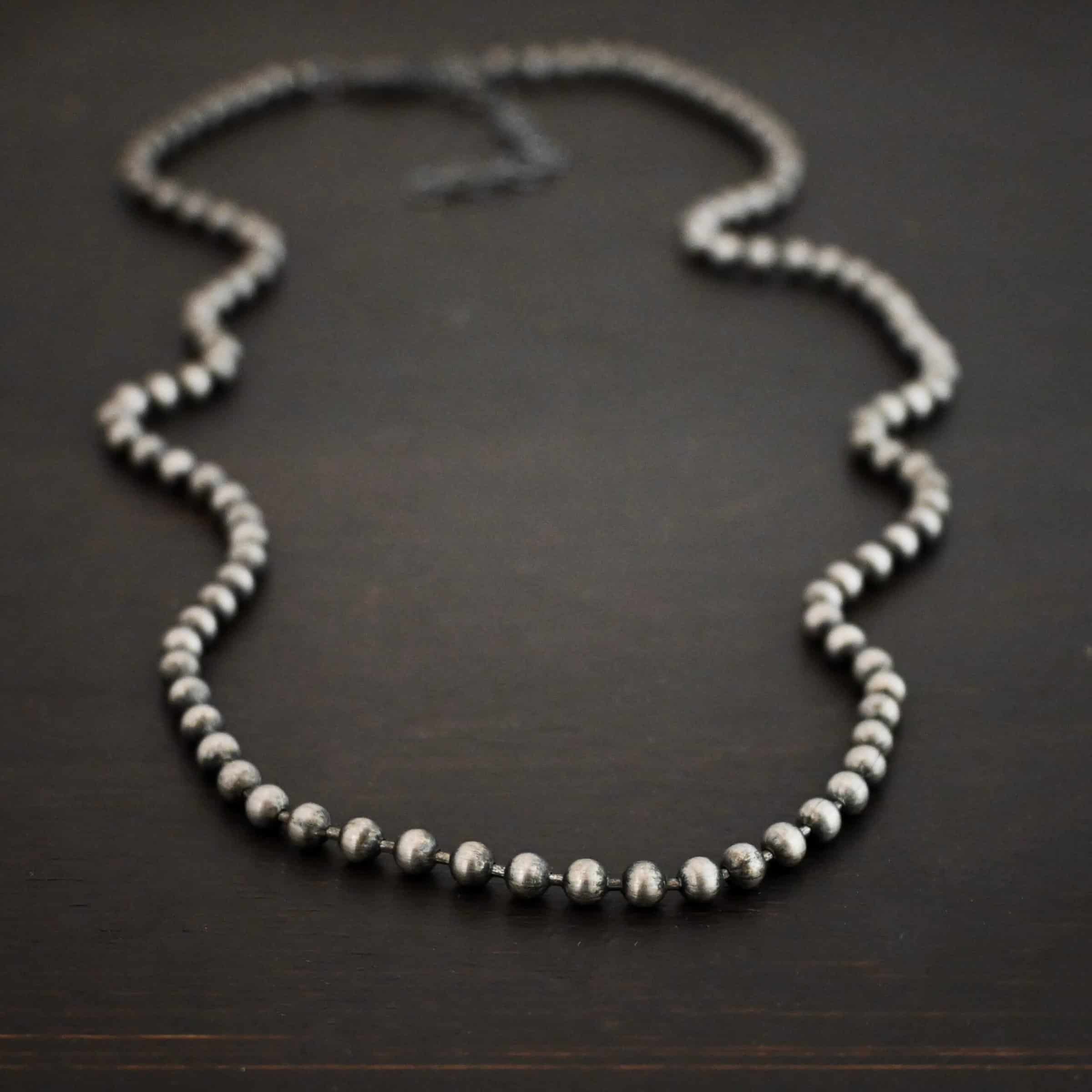 Beau Ball Chain Close up of the "Beau Ball" Chain. Made out of brushed stainless steel with 4mm balls that are spaced apart evenly on the chain. Chain is set against a dark background.