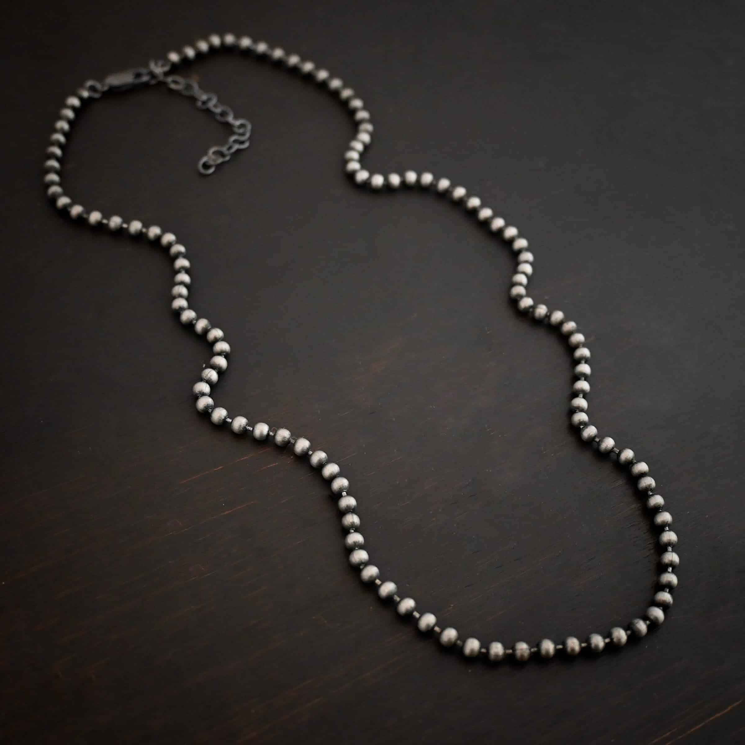 Beau Ball Chain Close up of the "Beau Ball" Chain. Made out of brushed stainless steel with 4mm balls that are spaced apart evenly on the chain. Chain is set against a dark background.