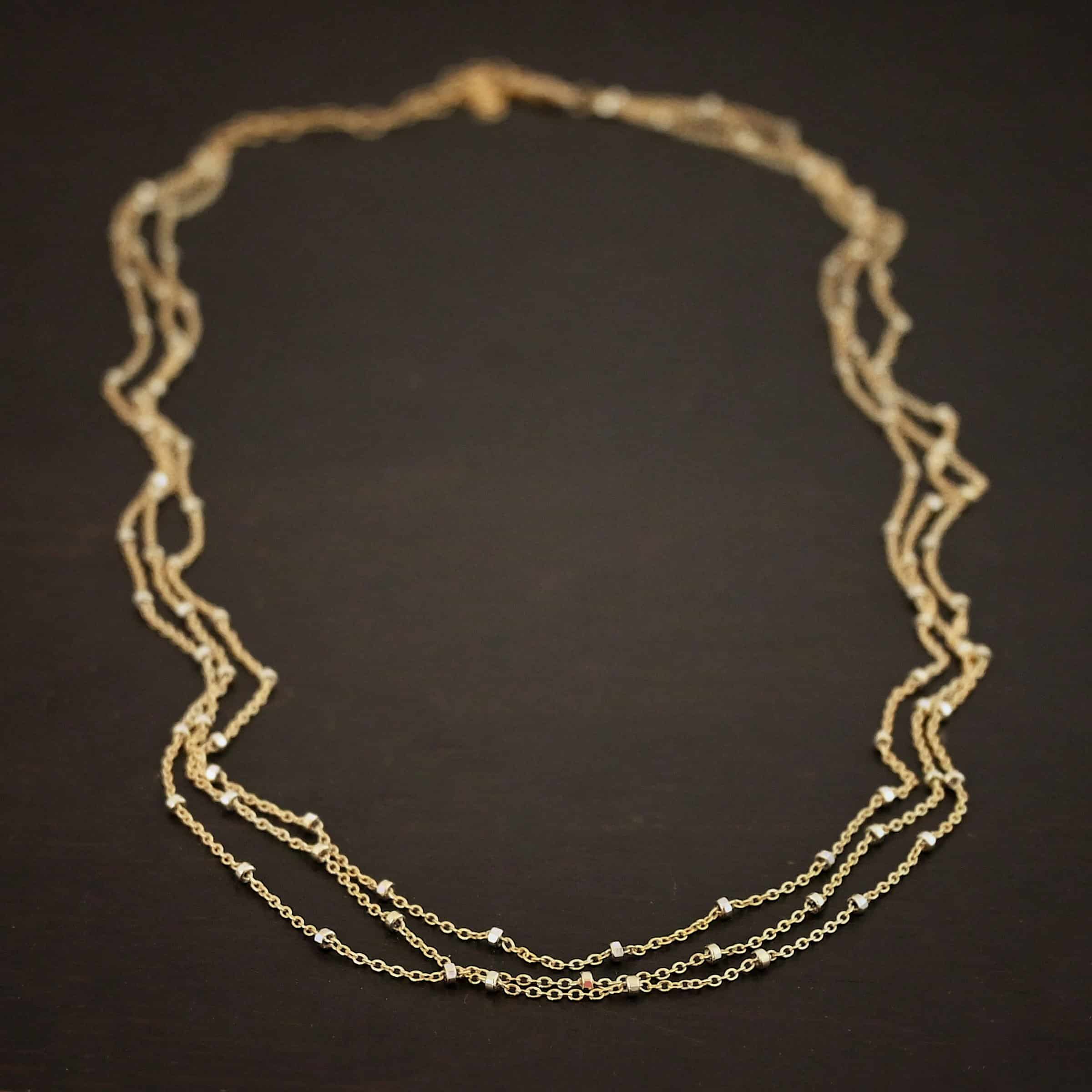 Morning in Paris Chain "Morning In Paris" Chain as shown up close. Gold Filled over Sterling Silver chain that is 1.2mm thick with 1.5mm beads. Chain is three separate strands that meet together at the back to form one chain. Chain is shown against a dark background.