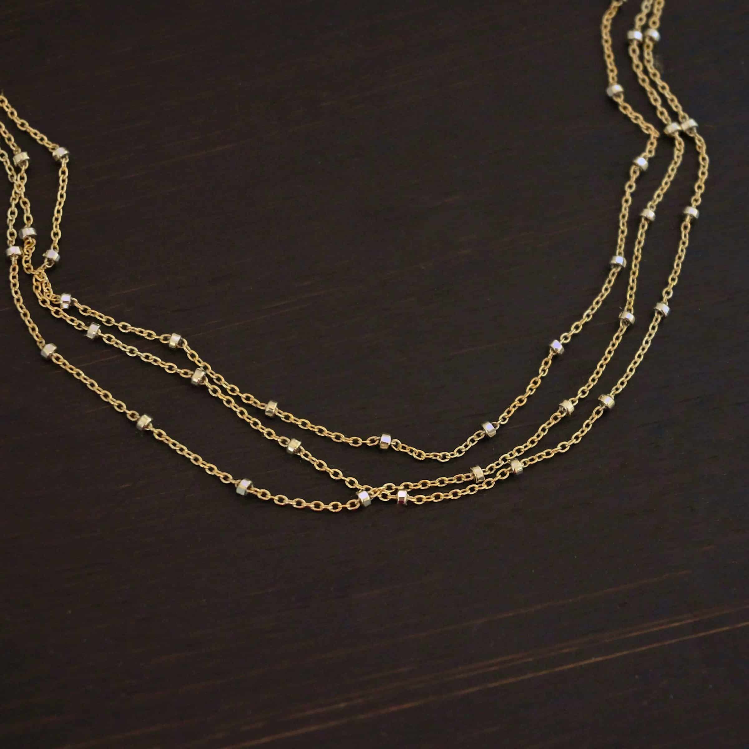 Morning in Paris Chain "Morning In Paris" Chain as shown up close. Gold Filled over Sterling Silver chain that is 1.2mm thick with 1.5mm beads. Chain is three separate strands that meet together at the back to form one chain. Chain is shown against a dark background.