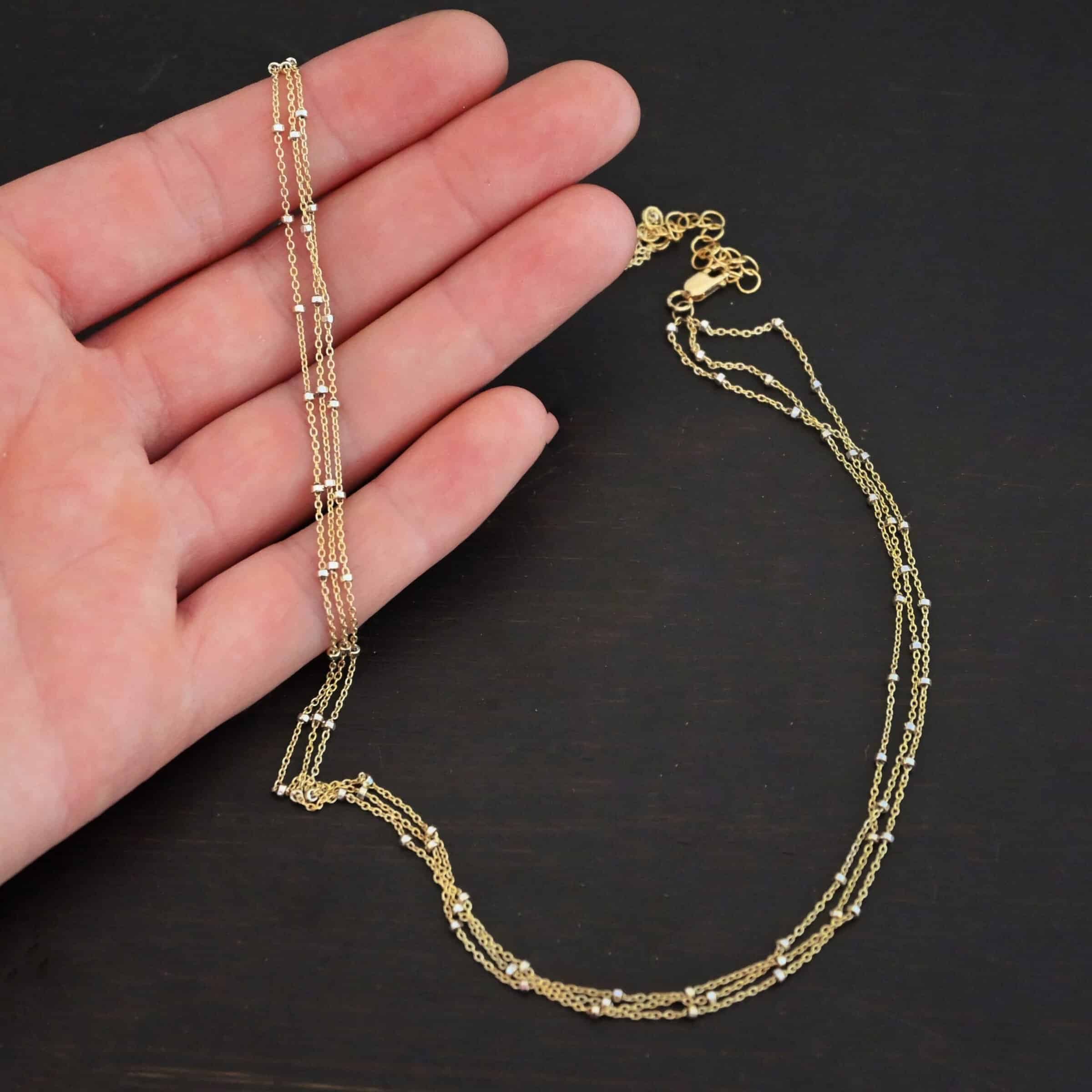 Morning in Paris Chain "Morning In Paris" Chain as shown up close. Gold Filled over Sterling Silver chain that is 1.2mm thick with 1.5mm beads. Chain is three separate strands that meet together at the back to form one chain. Chain is lying against the fingertips of a hand to demonstrate size.