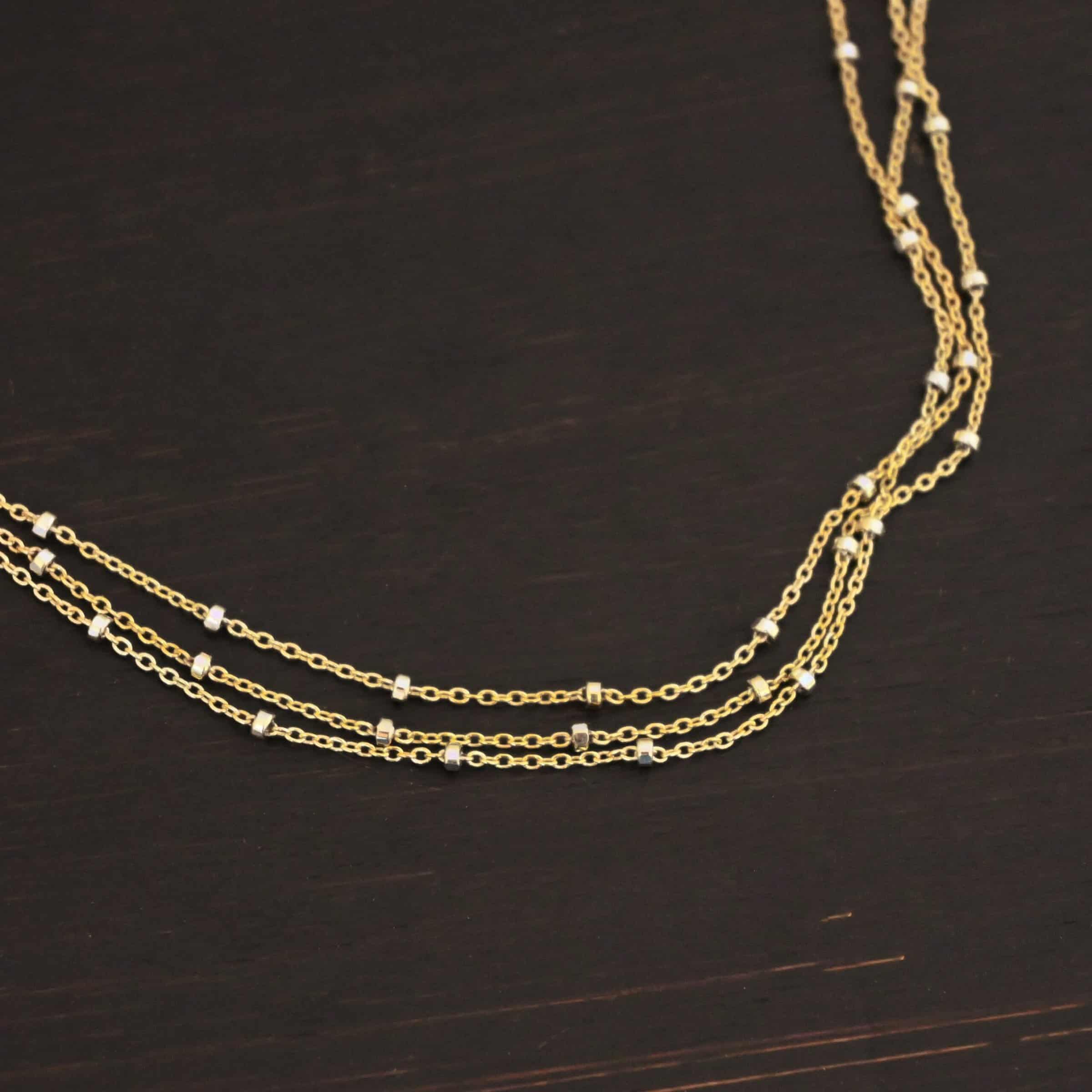 Morning in Paris Chain "Morning In Paris" Chain as shown up close. Gold Filled over Sterling Silver chain that is 1.2mm thick with 1.5mm beads. Chain is three separate strands that meet together at the back to form one chain. Chain is shown against a dark background.