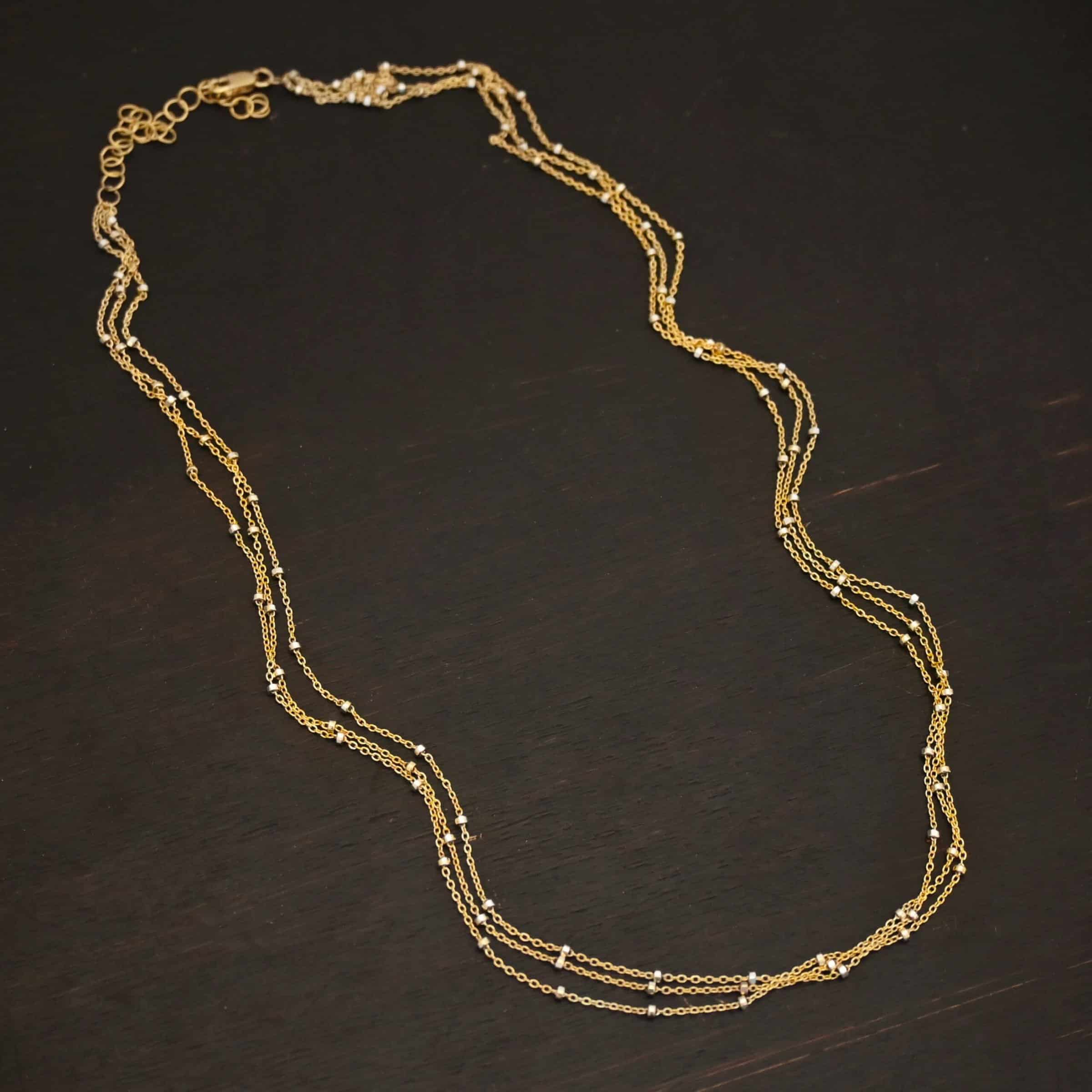 Morning in Paris Chain "Morning In Paris" Chain as shown up close. Gold Filled over Sterling Silver chain that is 1.2mm thick with 1.5mm beads. Chain is three separate strands that meet together at the back to form one chain. Chain is shown against a dark background.