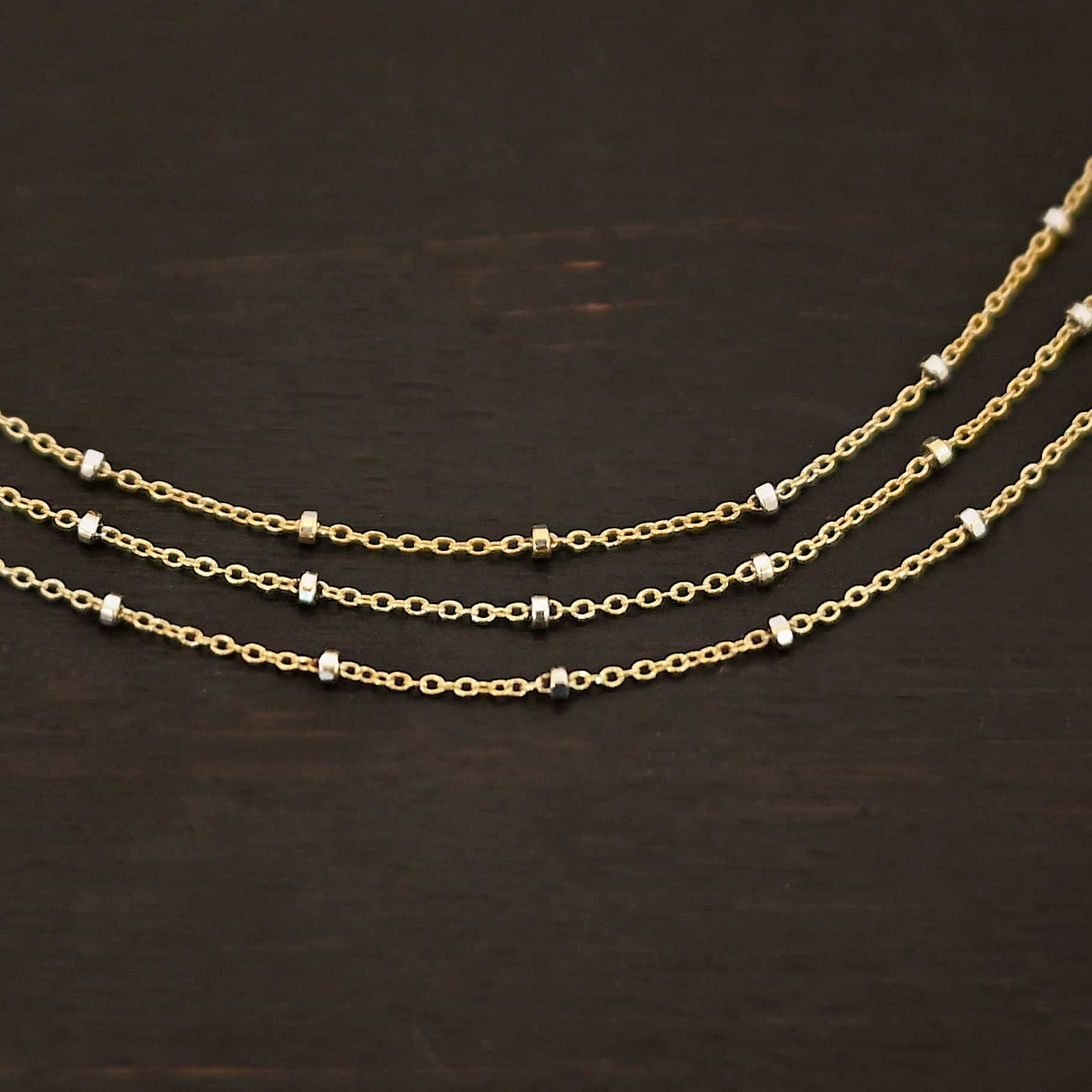 Morning in Paris Chain "Morning In Paris" Chain as shown up close. Gold Filled over Sterling Silver chain that is 1.2mm thick with 1.5mm beads. Chain is three separate strands that meet together at the back to form one chain. Chain is shown against a dark background.