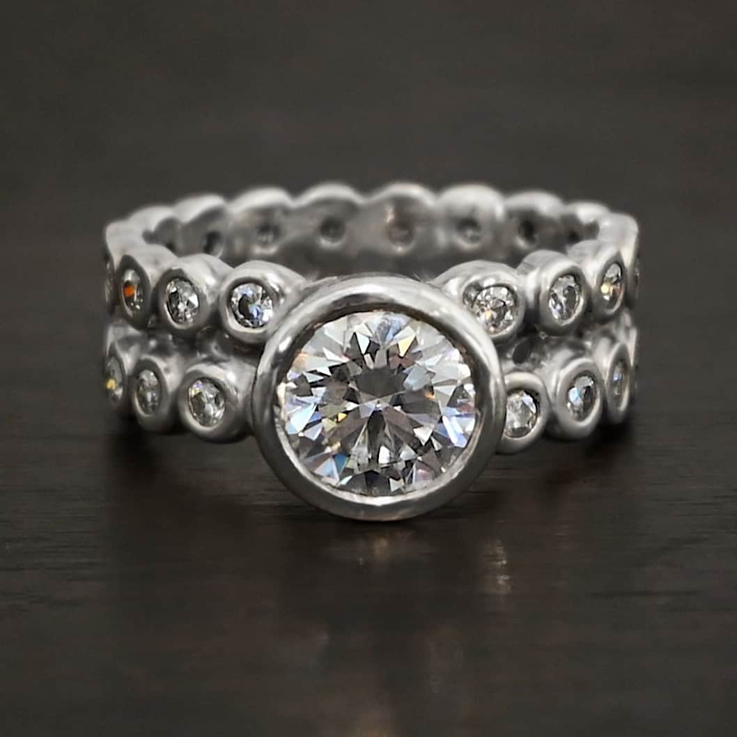 Heaven on Earth Ring Photo of the "Heaven On Earth" Ring. Made out of sterling silver and moissanites. There is a large moissanite in the center of the ring. The ring band is made of moissanites all the way around. There are two separate bands that are soldered together in the middle to create one band. Each band is made entirely out of moissanites that are set in silver and soldered together. Ring is sitting against a dark background.