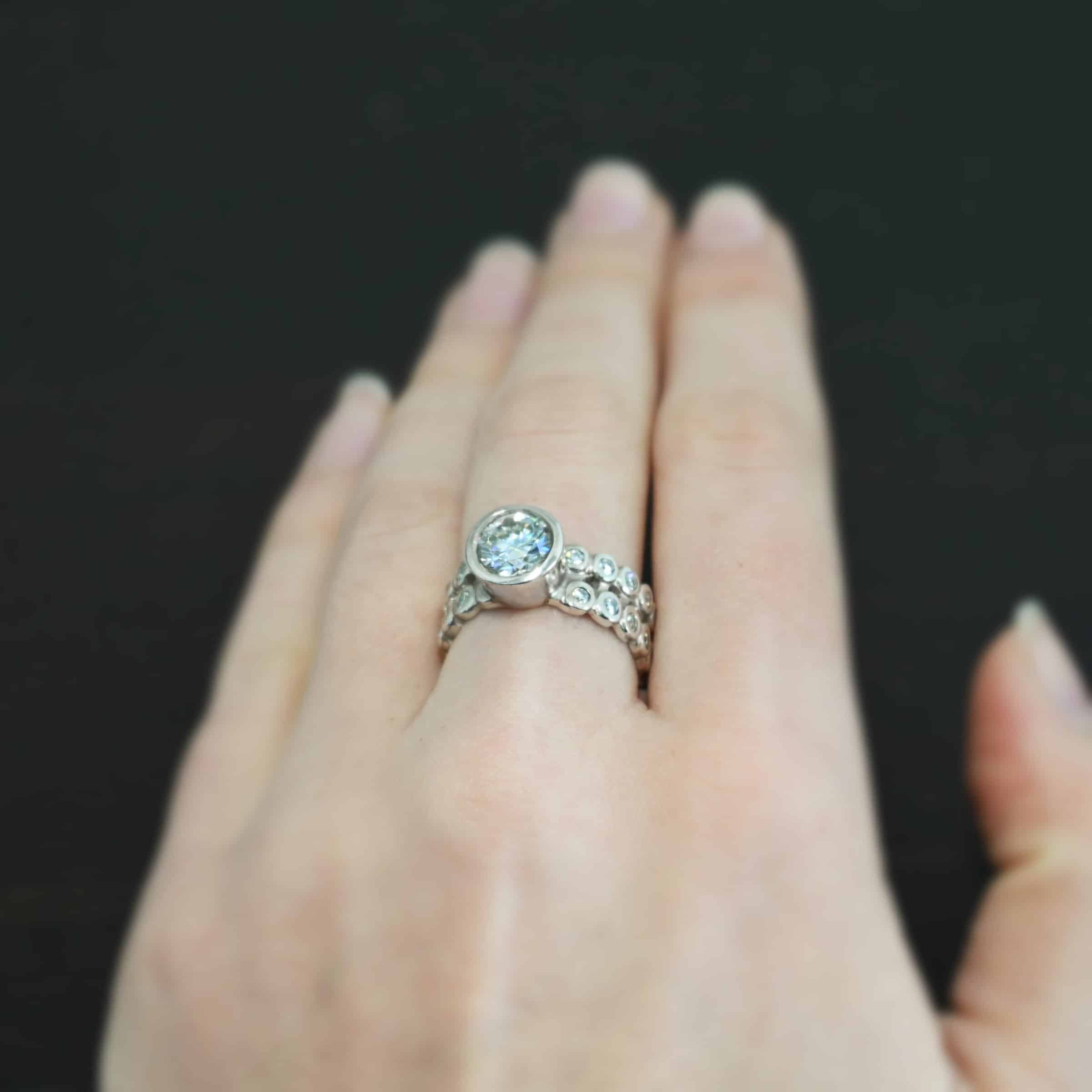 Heaven on Earth Ring Photo of the "Heaven On Earth" Ring. Made out of sterling silver and moissanites. There is a large moissanite in the center of the ring. The ring band is made of moissanites all the way around. There are two separate bands that are soldered together in the middle to create one band. Each band is made entirely out of moissanites that are set in silver and soldered together. Ring is worn by a model to demonstrate size.