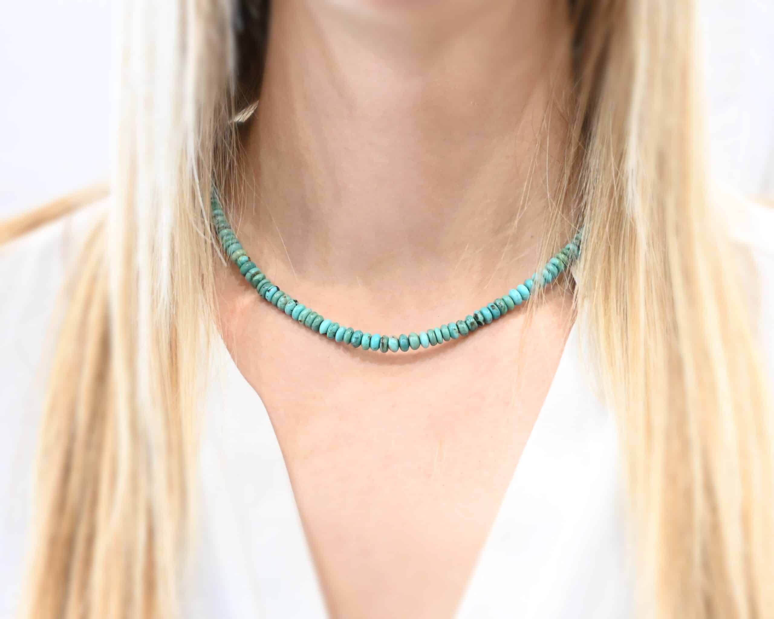 Photo of the "Hadley" Necklace. Made out of sterling silver and turquoise. The entire necklace has small, oval shaped turquoise beads strung around it. The ends of each side have two silver beads with crimps to keep the turquoise tight together. Necklace is worn by a model to demonstrate size.