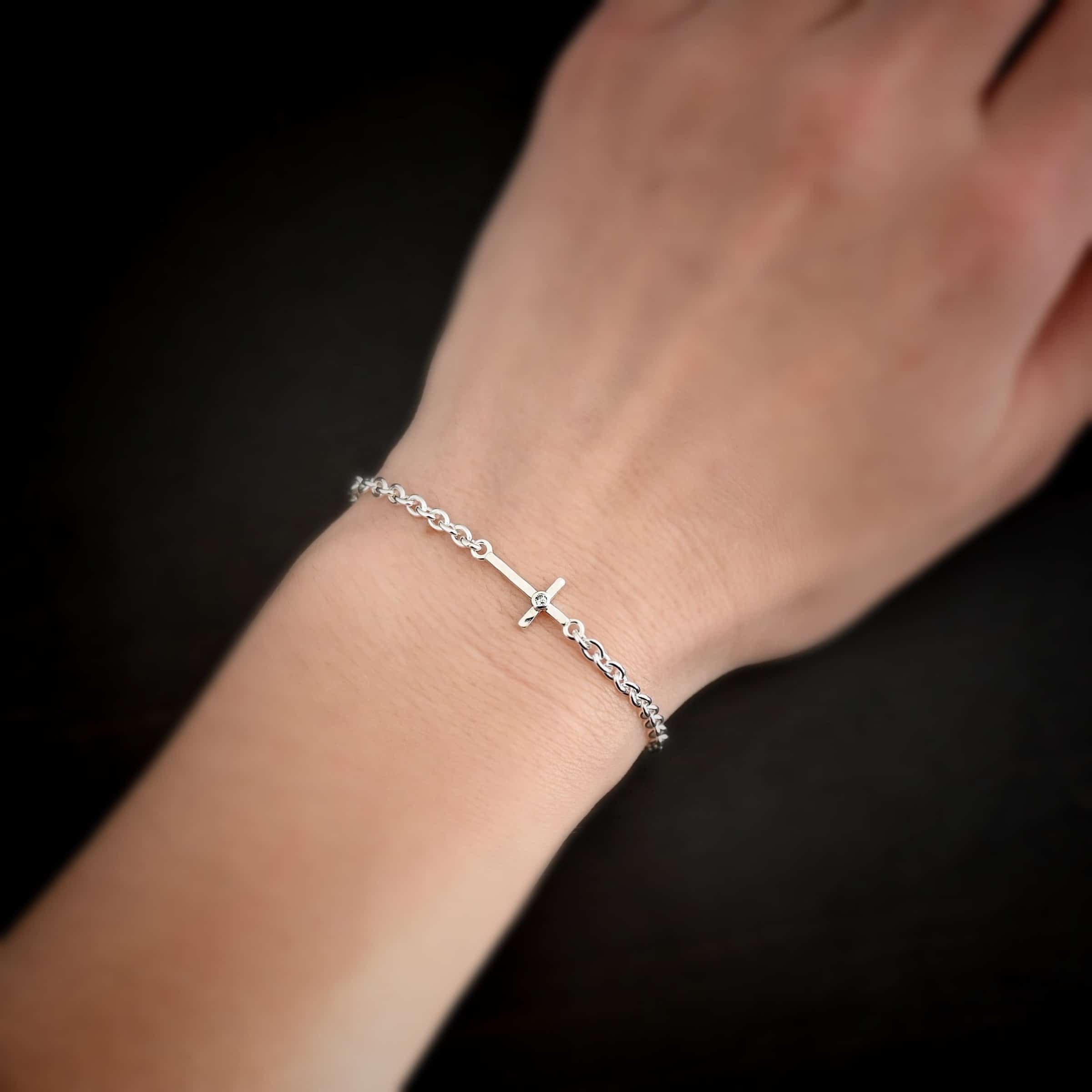 Photo of the "Creator" Bracelet. There is a cross set horizontally with a loop on each end. Each end of the cross is connected to each side of the chain in the center of the bracelet. There is a small cz in the center of the cross. The bracelet is shiny, and worn up close by a model on their wrist.
