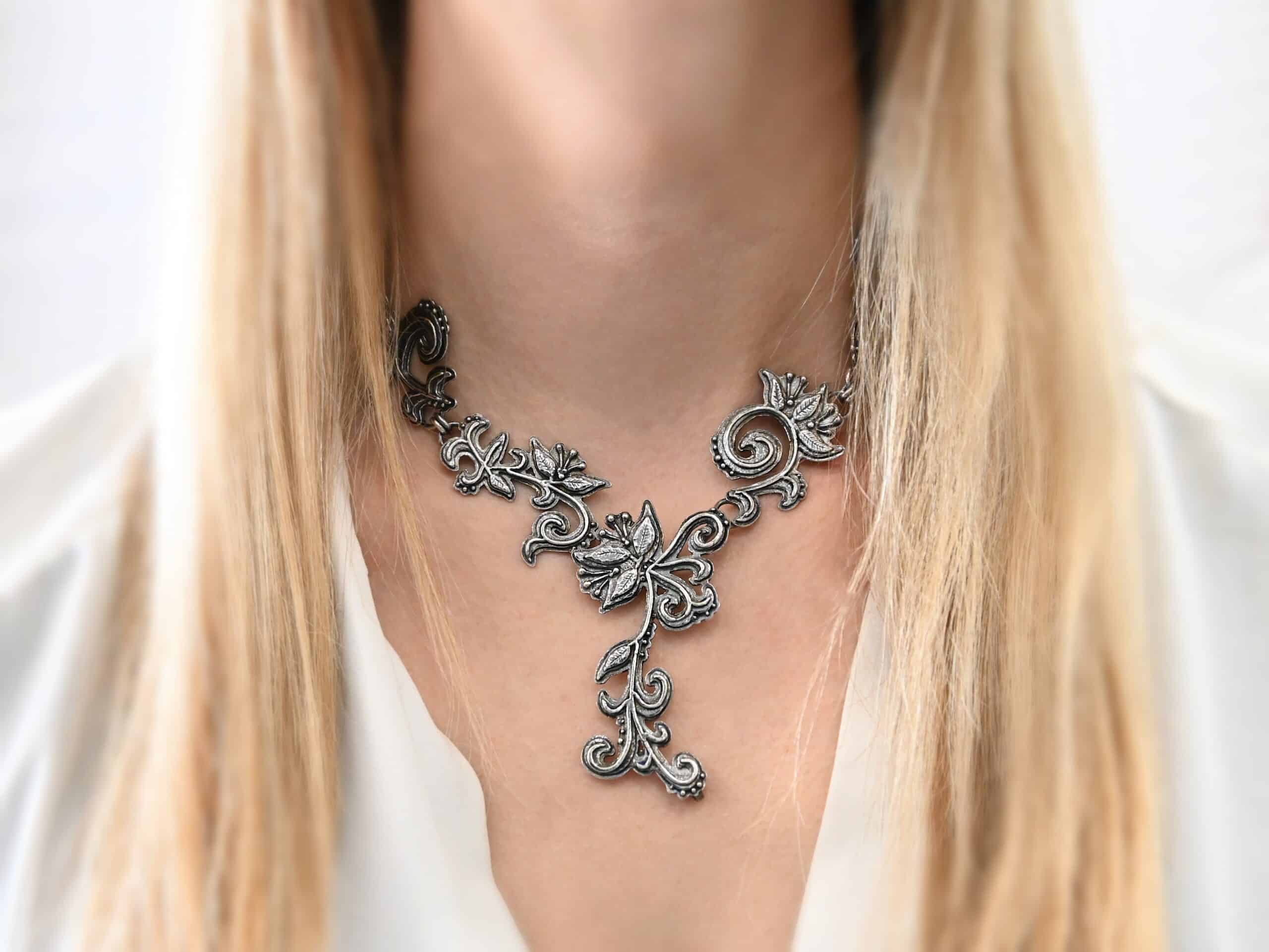 Paisley Necklace Photo of the "Paisley" Necklace. Made out of sterling silver. It is a large collar necklace. The entire necklace is made out of pendants that have sterling silver leaves and silver ball detail around the swirling pendants. The bottom of the necklace has a long, vine like pieces of silver that hangs down, with silver leaves at the top and in the center, and small swirls on the bottom. Necklace is worn by a model to demonstrate size.