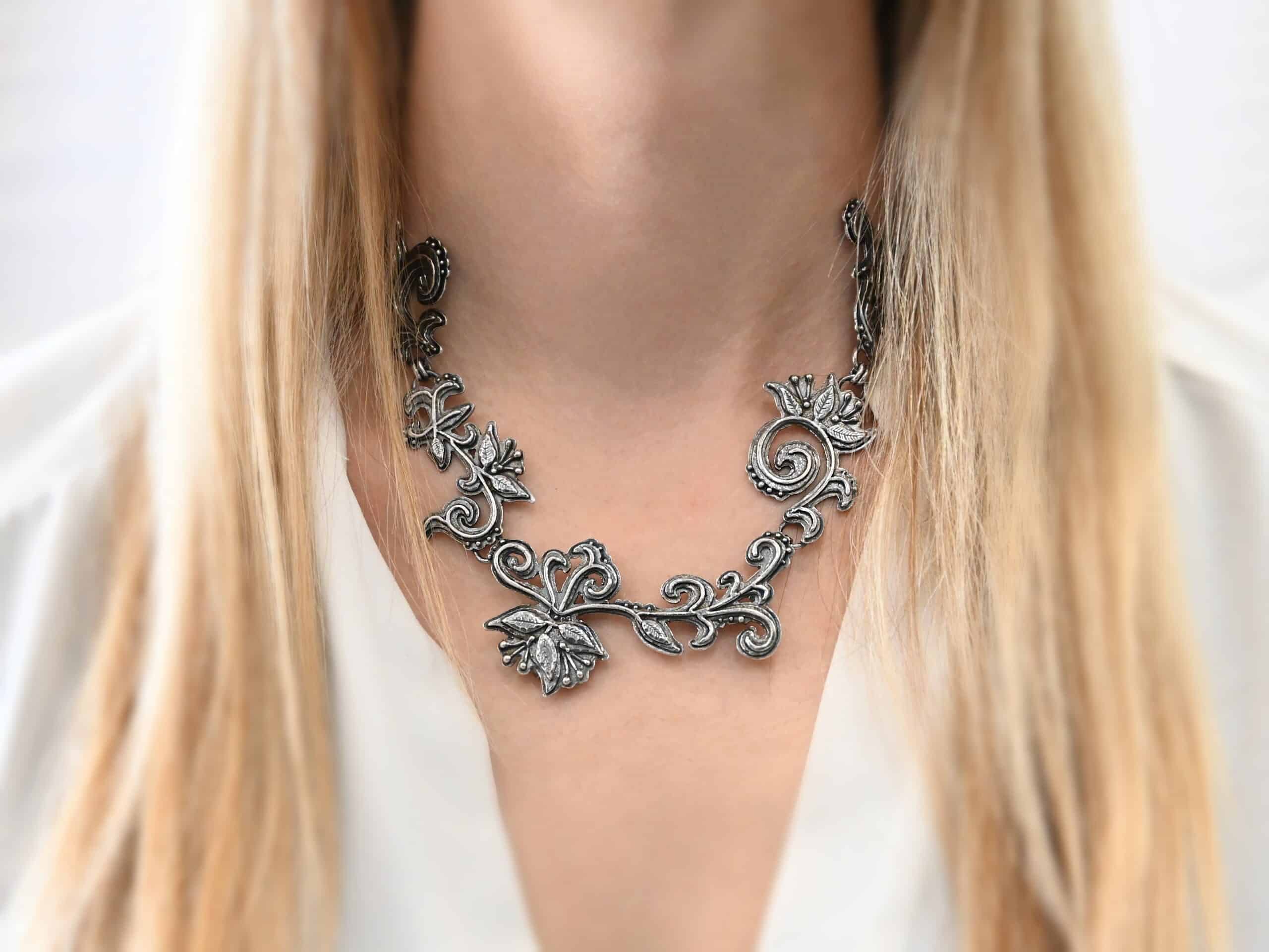 Paisley Necklace Photo of the "Paisley" Necklace. Made out of sterling silver. It is a large collar necklace. The entire necklace is made out of pendants that have sterling silver leaves and silver ball detail around the swirling pendants. The bottom of the necklace has a long, vine like pieces of silver that hangs down, with silver leaves at the top and in the center, and small swirls on the bottom. Necklace is worn by a model to demonstrate size.