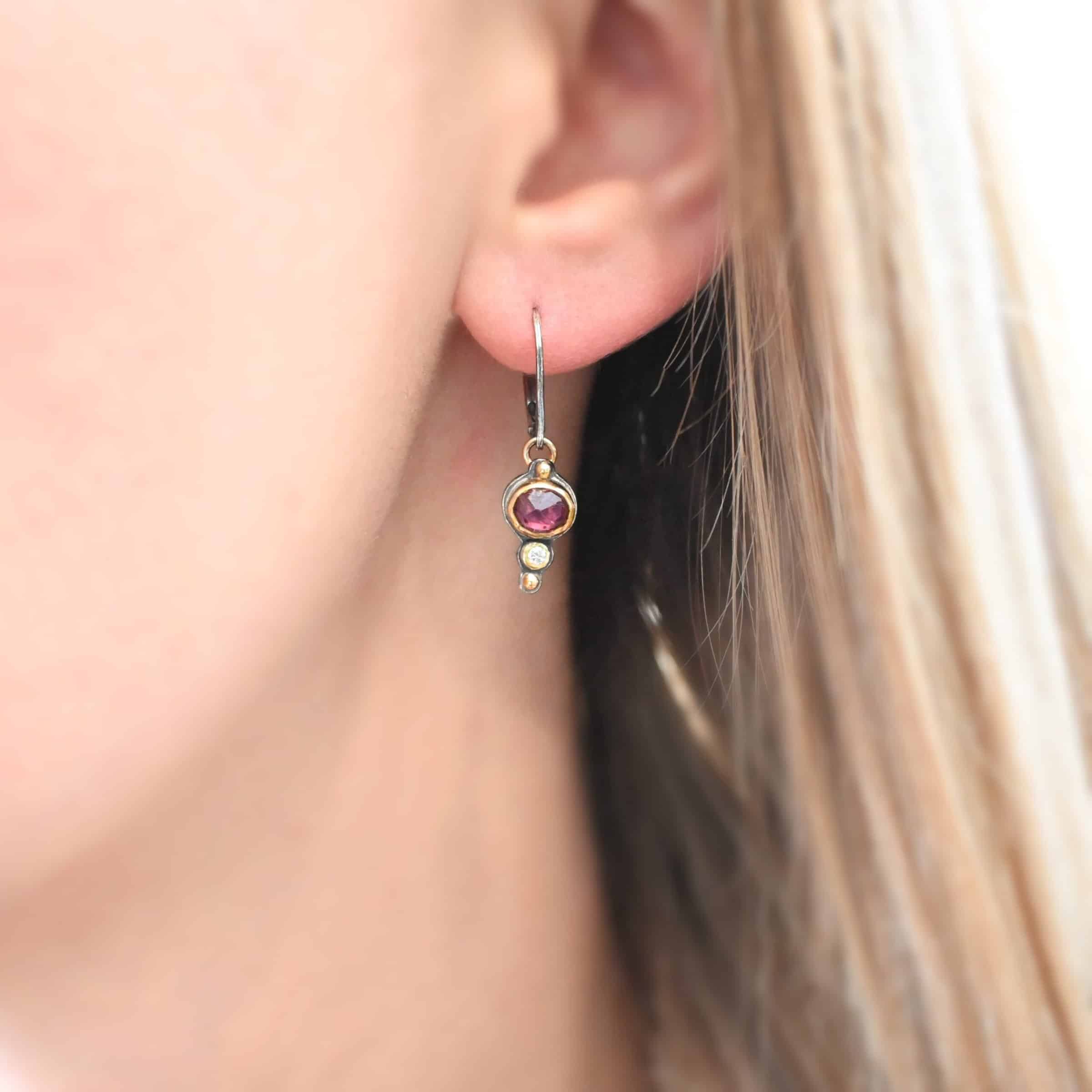 Champagne Blush Earrings Photo of the "Champagne Blush" Earring as shown on a model. Each earring has a ball of gold on the top, then an oval garnet, then a small diamond, and finally another ball of gold. The garnets and diamonds are set in gold. Earrings have sterling silver leverback ear wires.