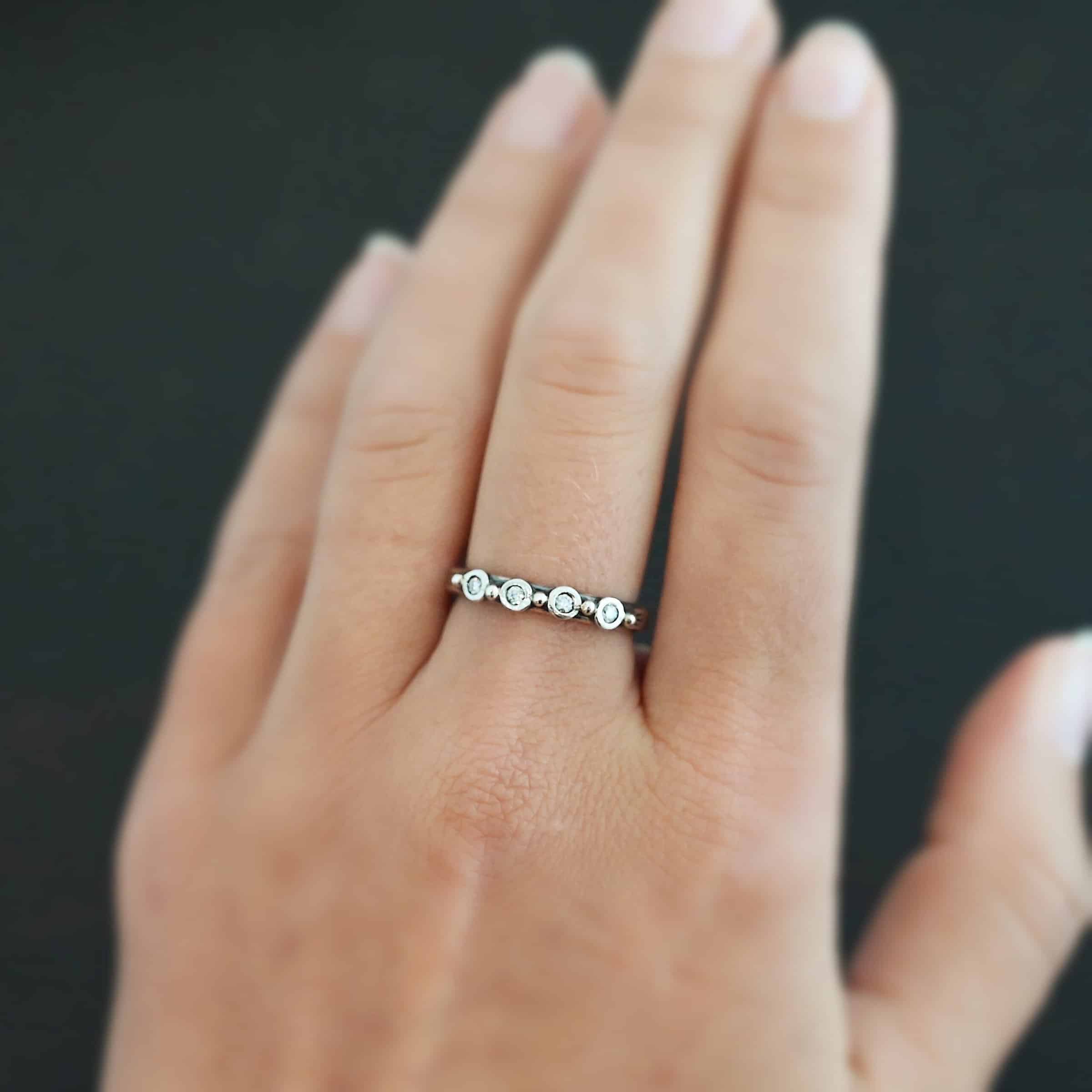 Photo of the "Years Of Love" Anniversary Band. It is a simple silver band with four diamonds across it. There are five silver balls on the band. Three are separating each diamond, and there is a silver ball before the first diamond and after the last diamond. Ring is worn on a models middle finger to demonstrate size.
