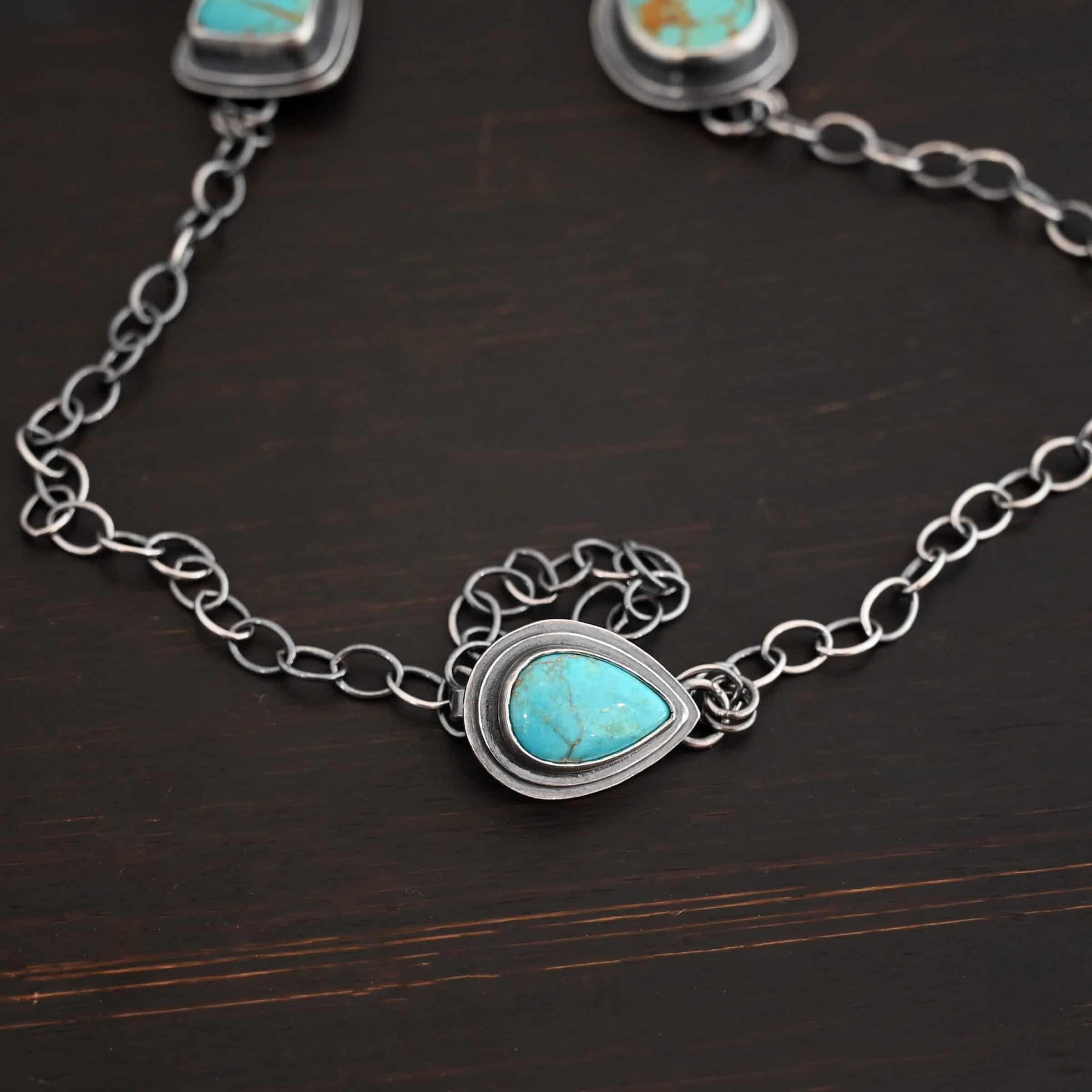 Gone with the Wind Necklace Clasp for the "Gone With The Wind" Necklace. Made out of sterling silver and turquoise. The turquoise is a teal color and a teardrop shape. The back of the clasp has loops in which the chain is attached to for the necklace. The turquoise is set in two layers of sterling silver. The top layer is smaller than the bottom layer, so both layers are noticeable.