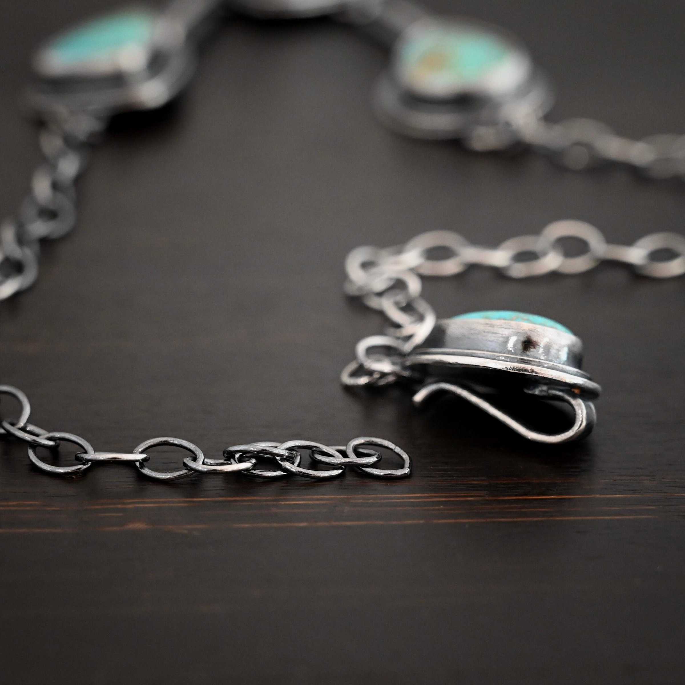 Gone with the Wind Necklace Clasp for the "Gone With The Wind" Necklace. Made out of sterling silver and turquoise. The turquoise is a teal color and a teardrop shape. The back of the clasp has loops in which the chain is attached to for the necklace. The turquoise is set in two layers of sterling silver. The top layer is smaller than the bottom layer, so both layers are noticeable. The clasp is not attached to the chain to show how the clasp works.