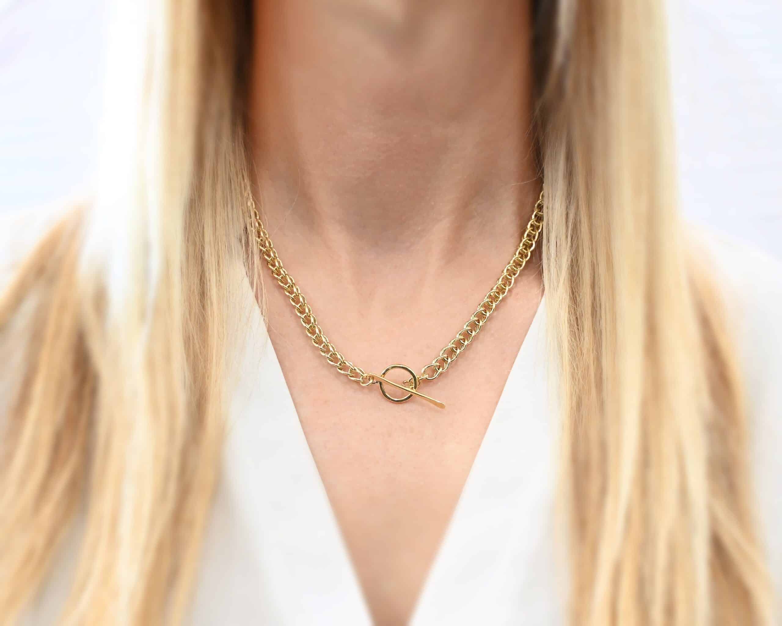 Gretchen Chain Photo of the "Gretchen" Chain. Chain is made out of 18k gold. Chain is a viking knit chain, and approximately 18" long. Chain has a toggle clasp. Chain is flipped around to show the clasp of the necklace. Necklace is worn by a model. Model is wearing a white v-neck shirt.