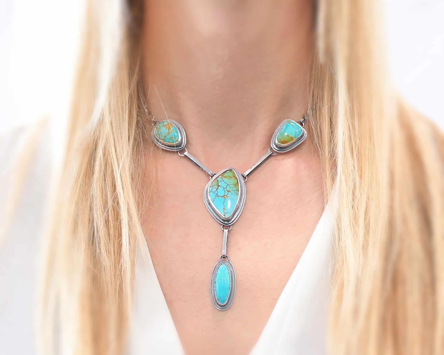 Gone with the Wind Necklace Photo of "Gone With The Wind" Necklace. This is a large turquoise necklace. The necklace has five turquoise, one on the left side, one on the right side, and two in the center. The two in the center are one on top of the other. There is a turquoise on the clasp of the necklace as well. Each turquoise is connected by a small silver bar and each bar is connected to loops on the backs of the settings for the turquoise. Necklace is worn by a model to demonstrate size.