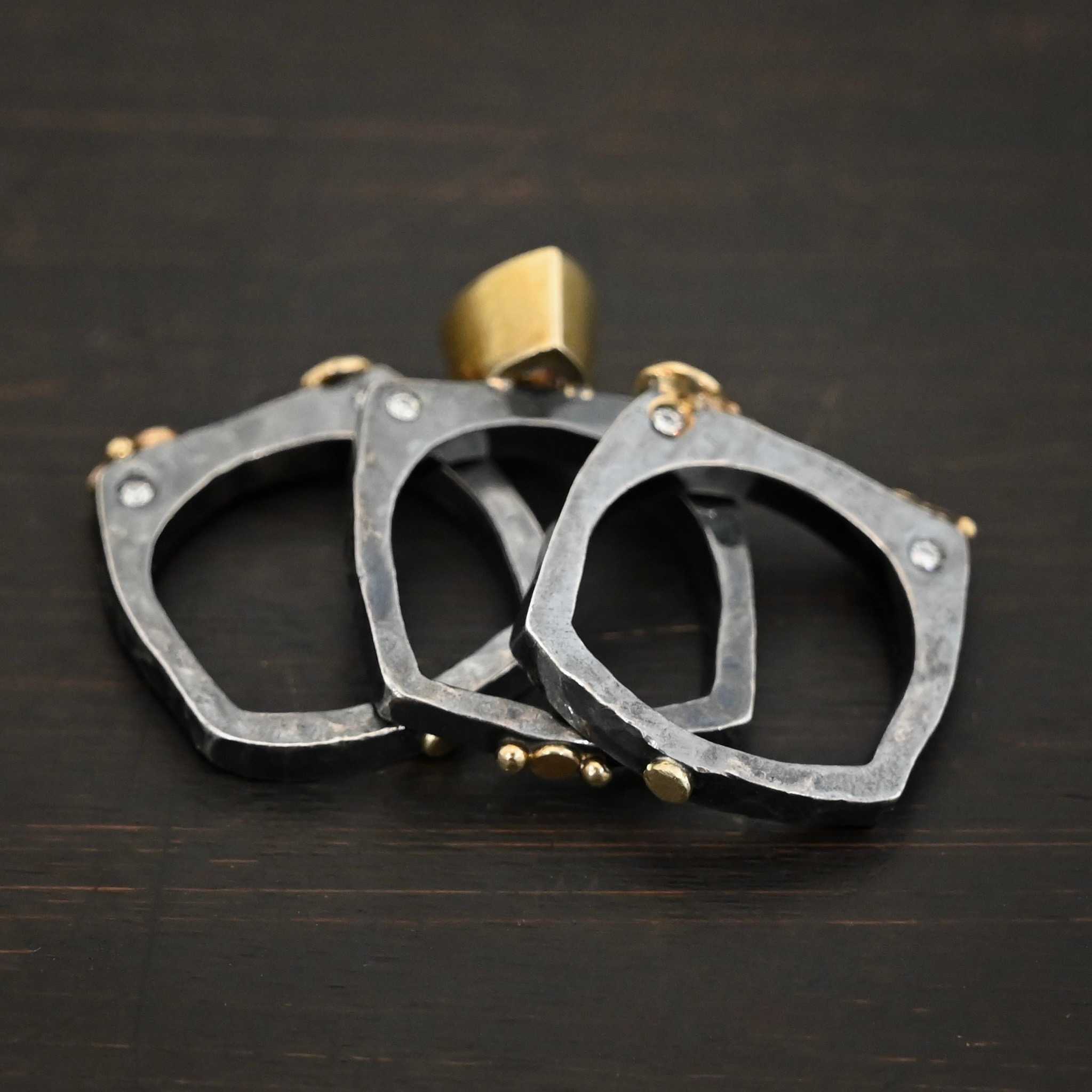 Photo of the back of the "Johnny & June" Ring. There are three smashed gold dots scattered across all three rings, and there are two gold balls in the center of the center ring. All three bands are separated and laying on top of one another against a dark background.