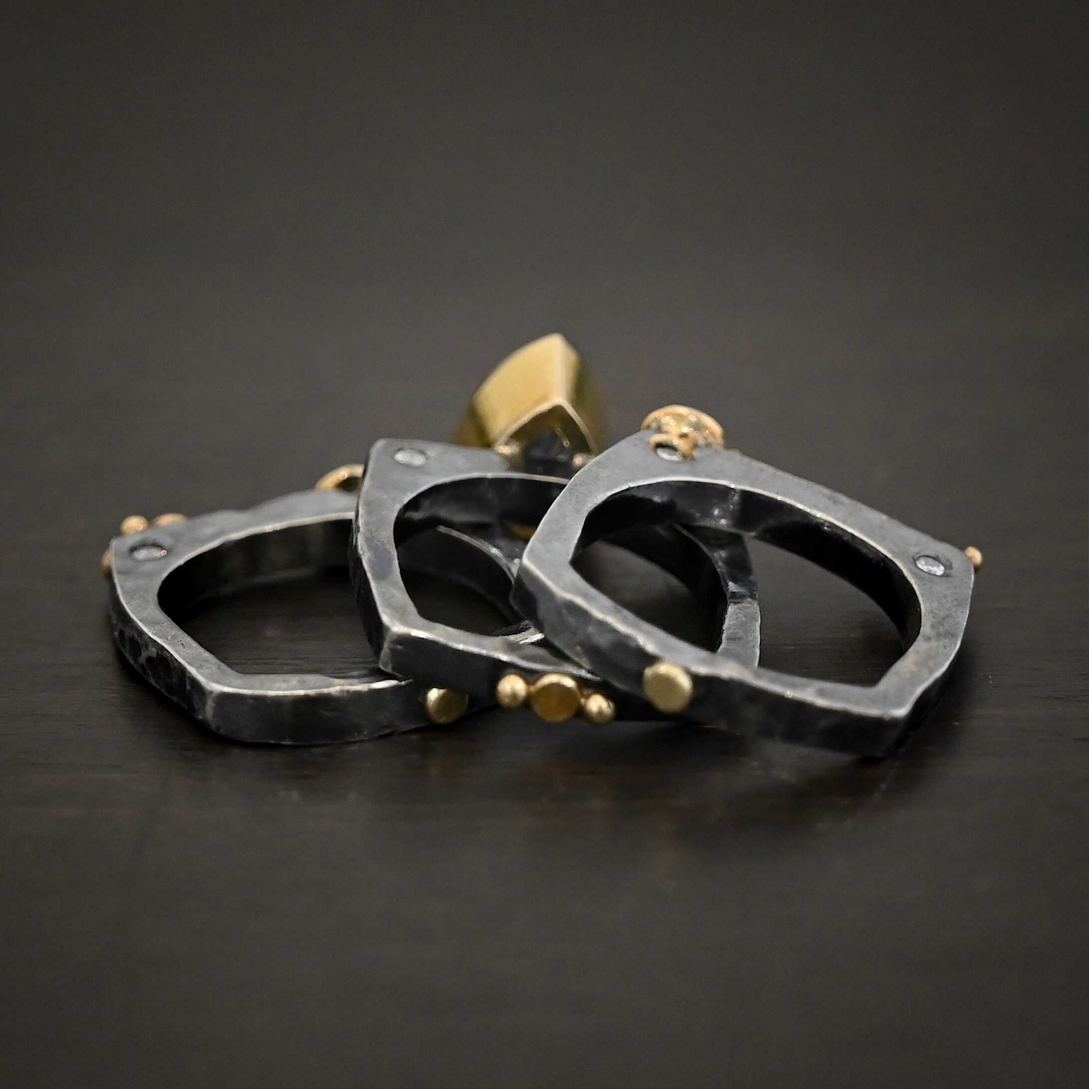 Photo of the back of the "Johnny & June" Ring. There are three smashed gold dots scattered across all three rings, and there are two gold balls in the center of the center ring. All three bands are separated and laying on top of one another against a dark background.