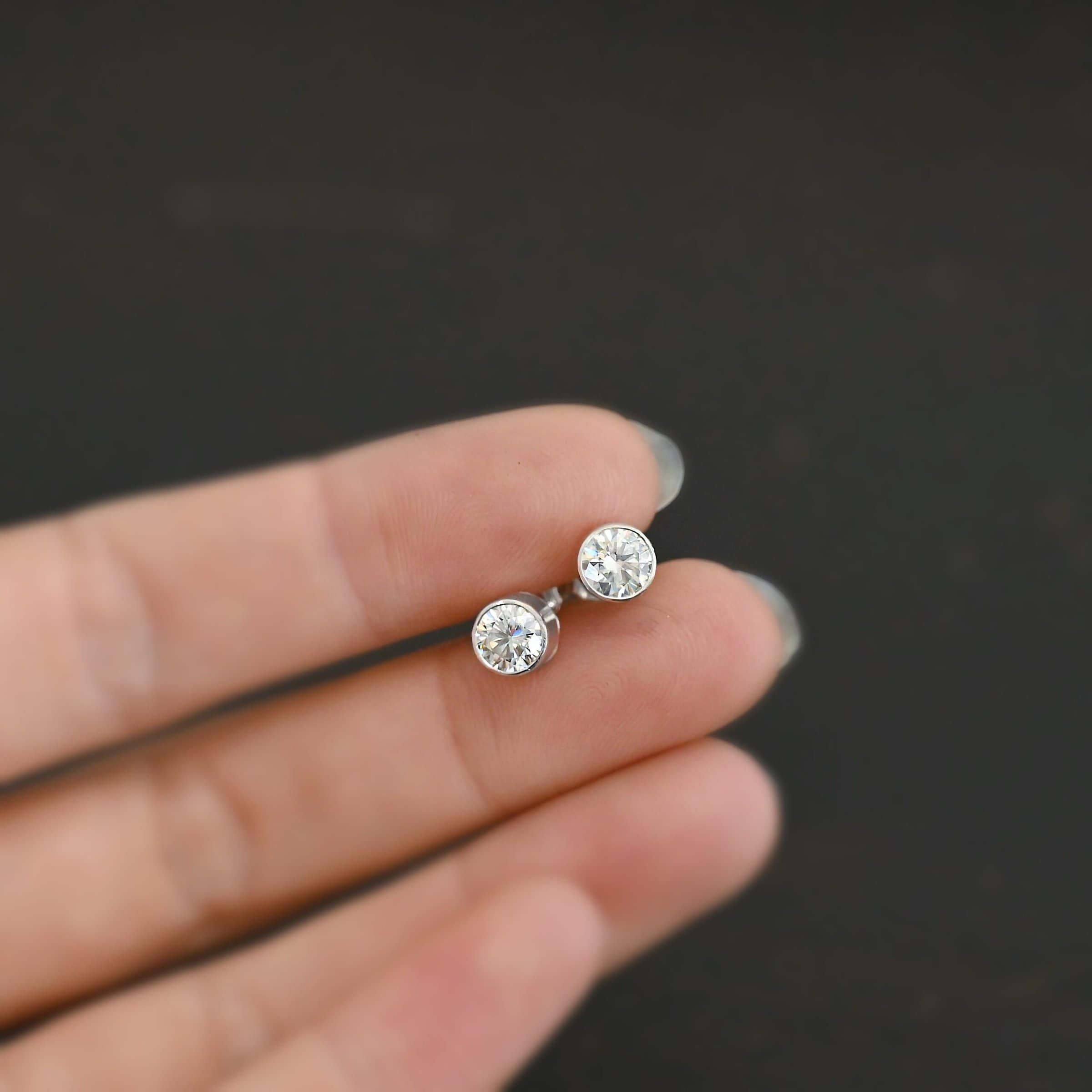 Photo of the "Betina" Earrings. Made out of sterling silver and moissanites. Each earring has a moissanite in the center that is set in sterling silver. Earrings are laying against the fingertips of a models hand to demonstrate size.
