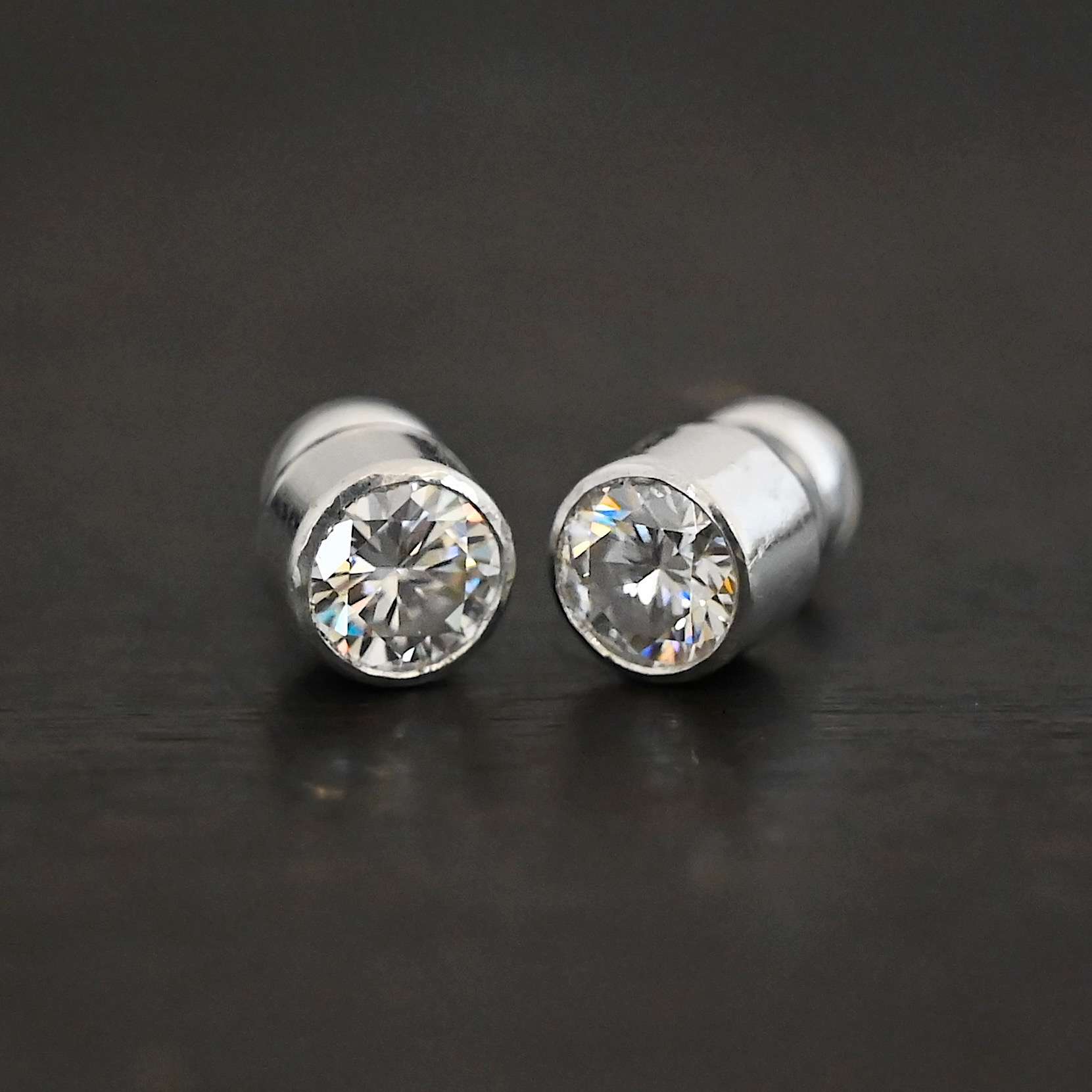 Photo of the "Betina" Earrings. Made out of sterling silver and moissanites. Each earring has a moissanite in the center that is set in sterling silver. Earrings are laying against a dark background.