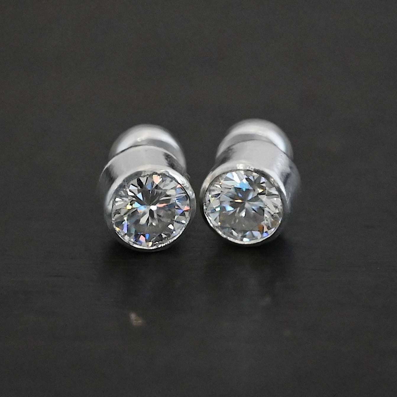 Photo of the "Betina" Earrings. Made out of sterling silver and moissanites. Each earring has a moissanite in the center that is set in sterling silver. Earrings are laying against a dark background.