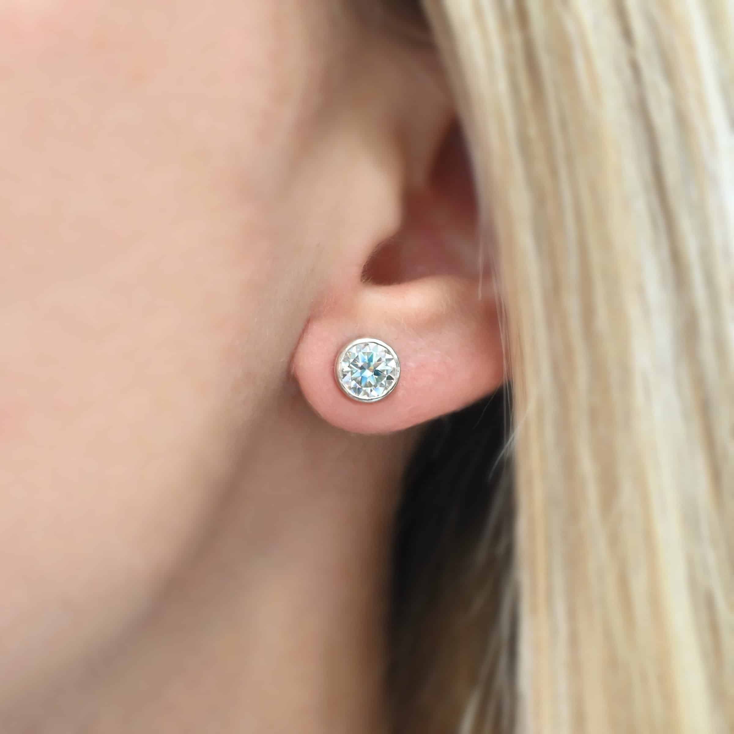 Photo of the "Betina" Earrings. Made out of sterling silver and moissanites. Earrings are sterling silver post earrings with moissanites in the center of them. The settings for the moissanites are thick and the posts are on the back center of the setting. Earrings are worn on a model to demonstrate size.
