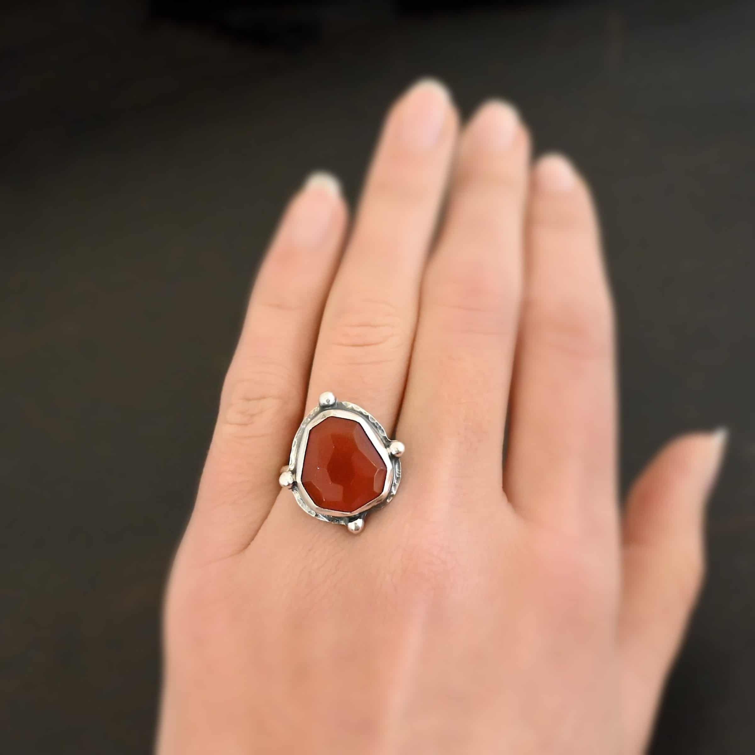 Cindy Lou Ring Photo of the "Cindy Lou" Ring. Made out of sterling silver and carnelian. The carnelian is a deep orange color and rose cut. The silver setting around it is hammered. On each side of the carnelian is a silver dot. One on the top, one on each side, and one on the bottom. Ring is worn on a models engagement ring finger to demonstrate size.