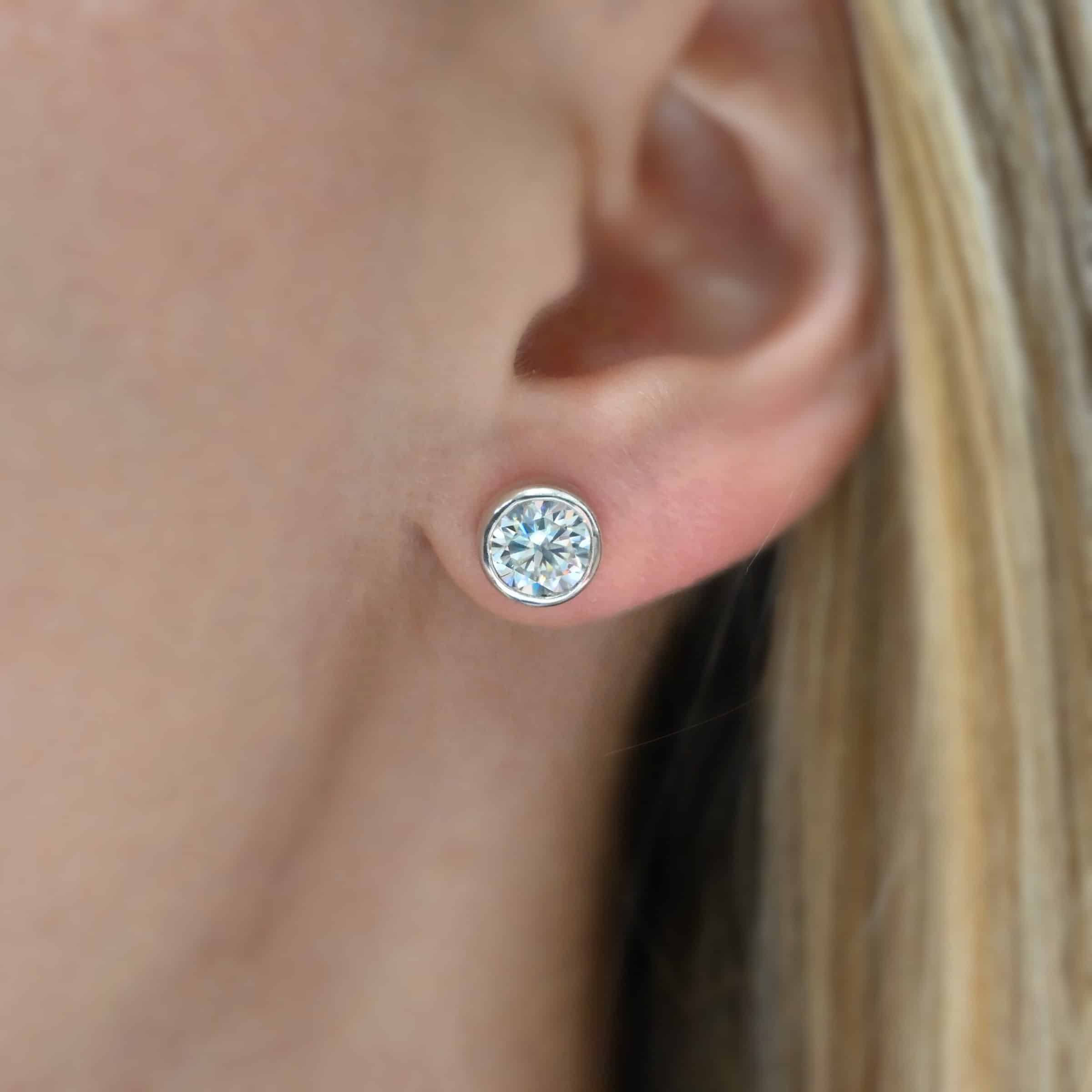 Photo of the "Betina" Earrings. Made out of sterling silver and moissanites. Earrings are sterling silver post earrings with moissanites in the center of them. The settings for the moissanites are thick and the posts are on the back center of the setting. Earrings are worn by a model to demonstrate size.