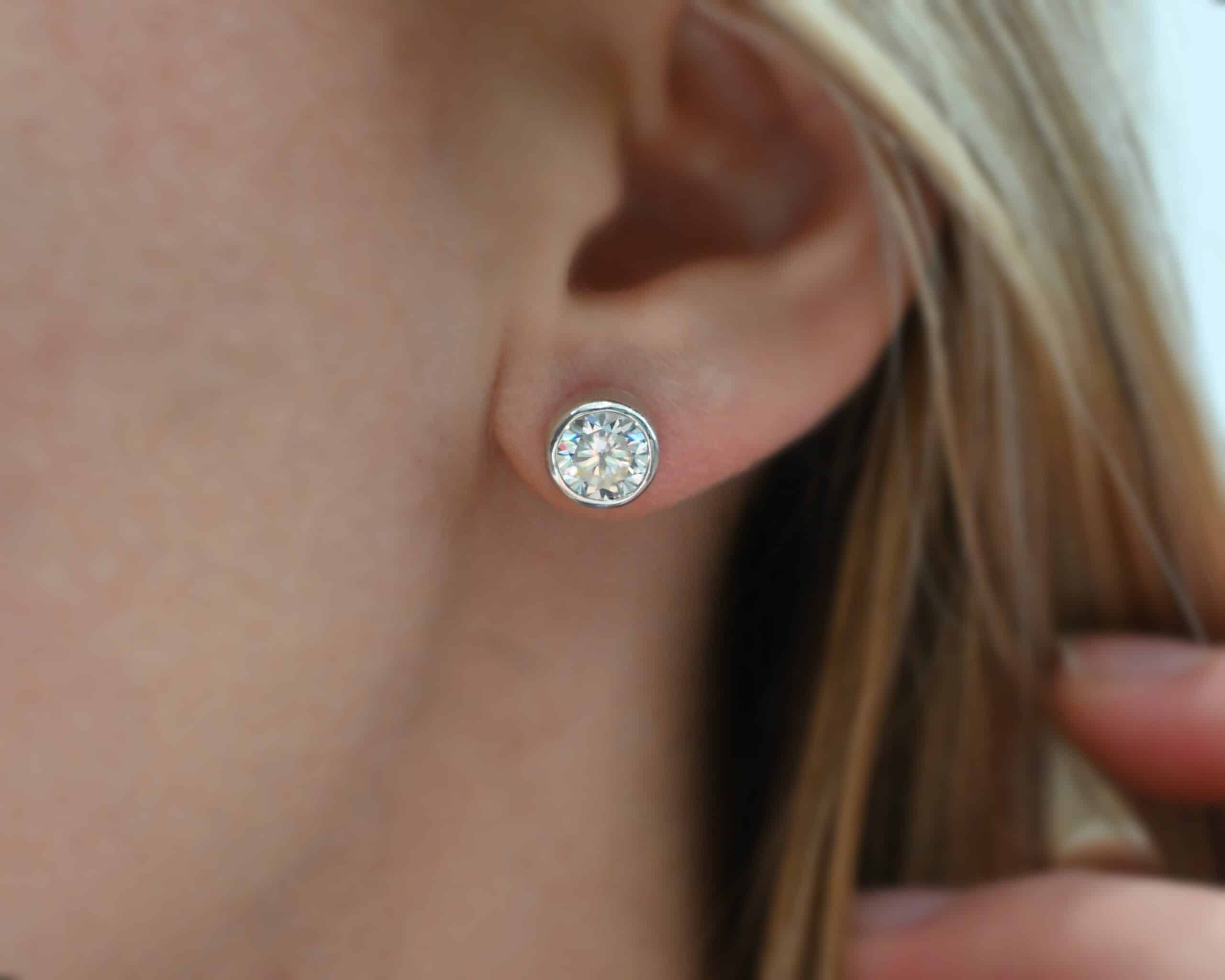Photo of the "Betina" Earrings. Made out of sterling silver and moissanites. Earrings are sterling silver post earrings with moissanites in the center of them. The settings for the moissanites are thick and the posts are on the back center of the setting. Earrings are worn by a model to demonstrate size.