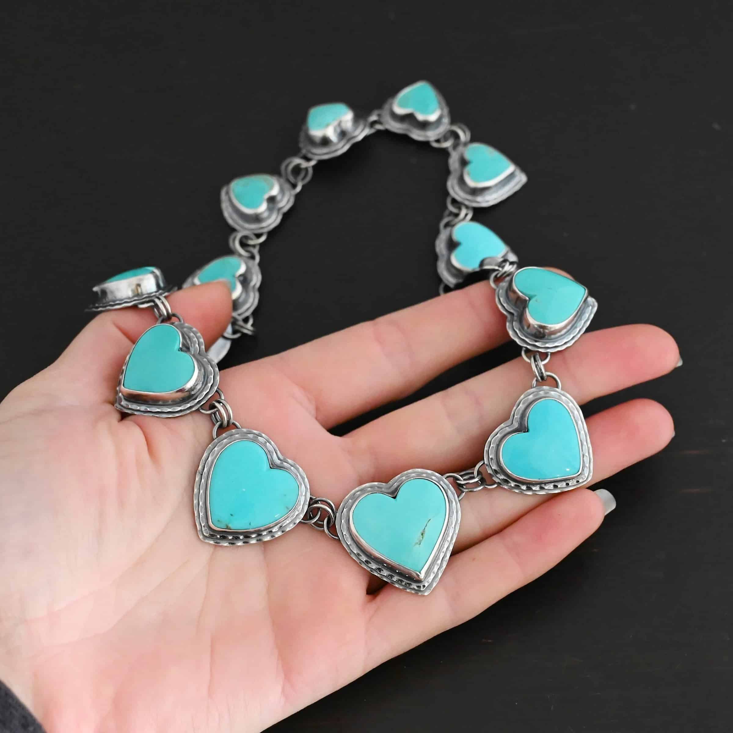 Heart & Soul Necklace Close up of the "Heart & Soul" Necklace. Made out of sterling silver and turquoise. There are fourteen turquoise hearts that circle around and create a collar necklace. Each turquoise heart is a light teal color and is set in sterling silver. Necklace is laying the fingertips of a hand to demonstrate size.