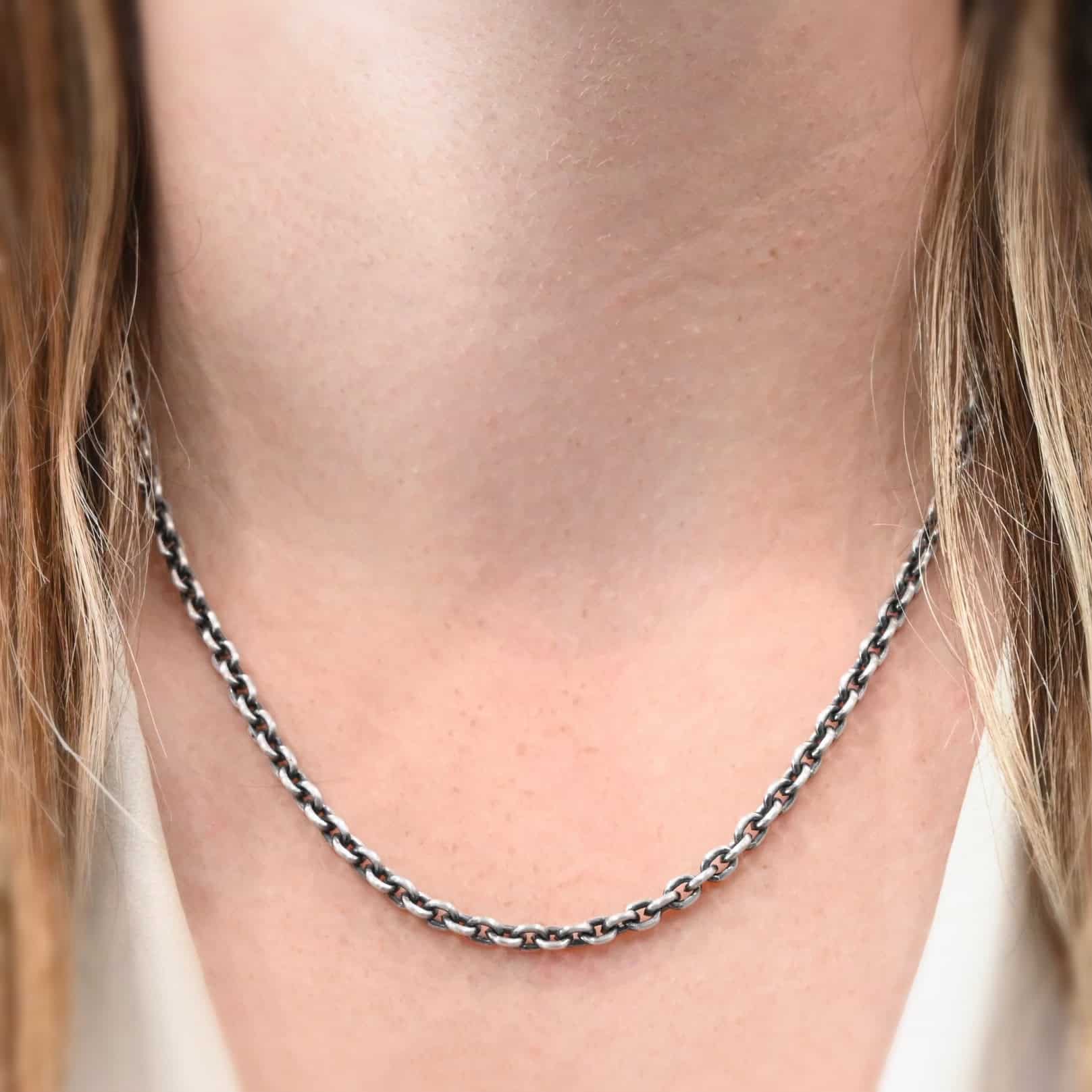 Joan Chain 18-21" oxidized "Joan" Chain at 18 inches shown by a model. Made out of sterling silver and oxidized. Links measure 6x5mmx1.2mm thick. Model is wearing a white v-neck shirt.