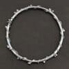 Close up of the "Ice Berry" Bangle. Made out of sterling silver and oxidized. Bangle has sterling silver "vines" wrapped all the way around it with small silver balls that are scattered around the bangle and vines. Bangle is laying against a dark background.