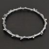Close up of the "Ice Berry" Bangle. Made out of sterling silver and oxidized. Bangle has sterling silver "vines" wrapped all the way around it with small silver balls that are scattered around the bangle and vines. Bangle is laying against a dark background.
