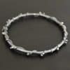 Close up of the "Ice Berry" Bangle. Made out of sterling silver and oxidized. Bangle has sterling silver "vines" wrapped all the way around it with small silver balls that are scattered around the bangle and vines. Bangle is laying against a dark background.